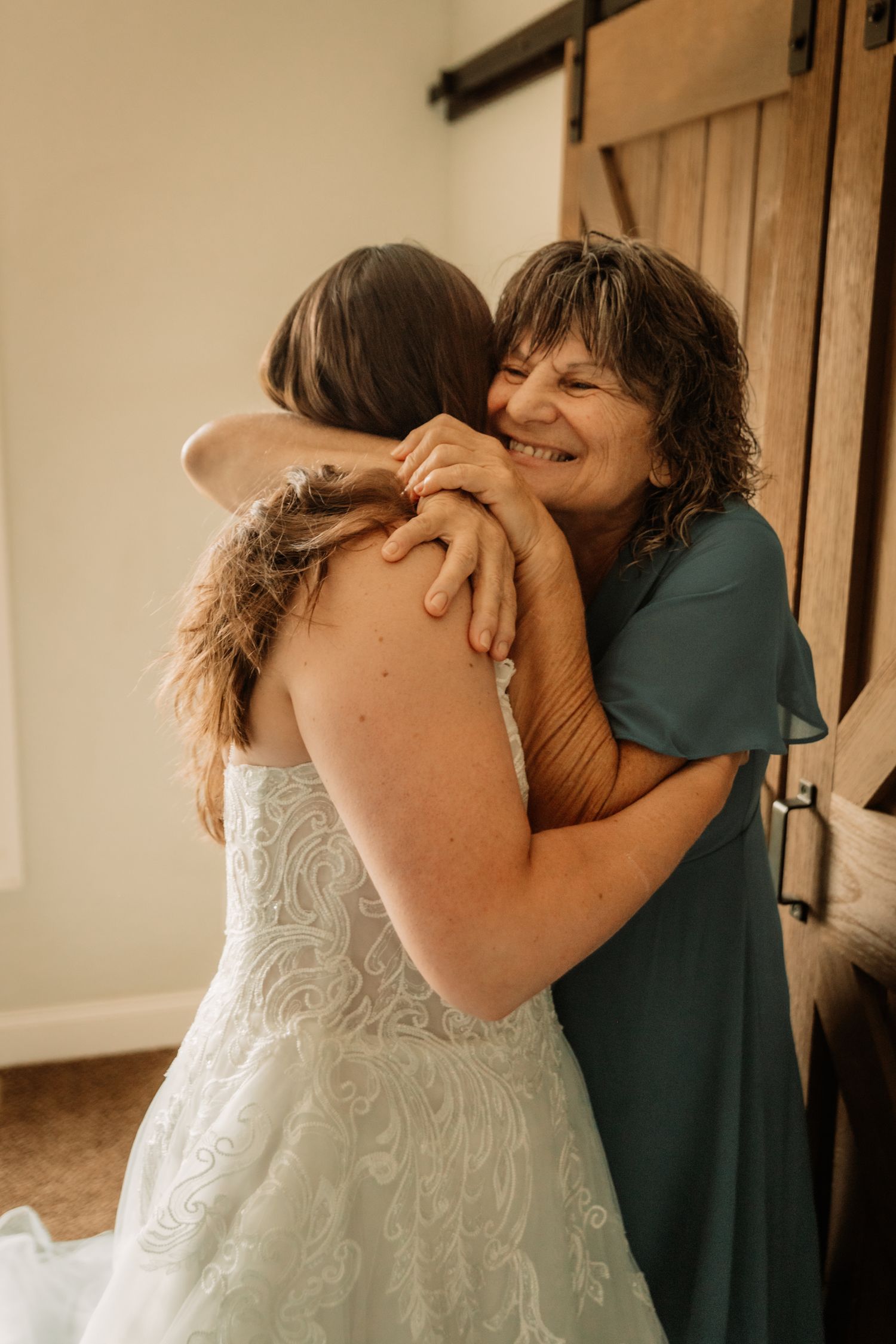 Two people share an emotional embrace at what appears to be a wedding, with one wearing a white lace bridal gown.