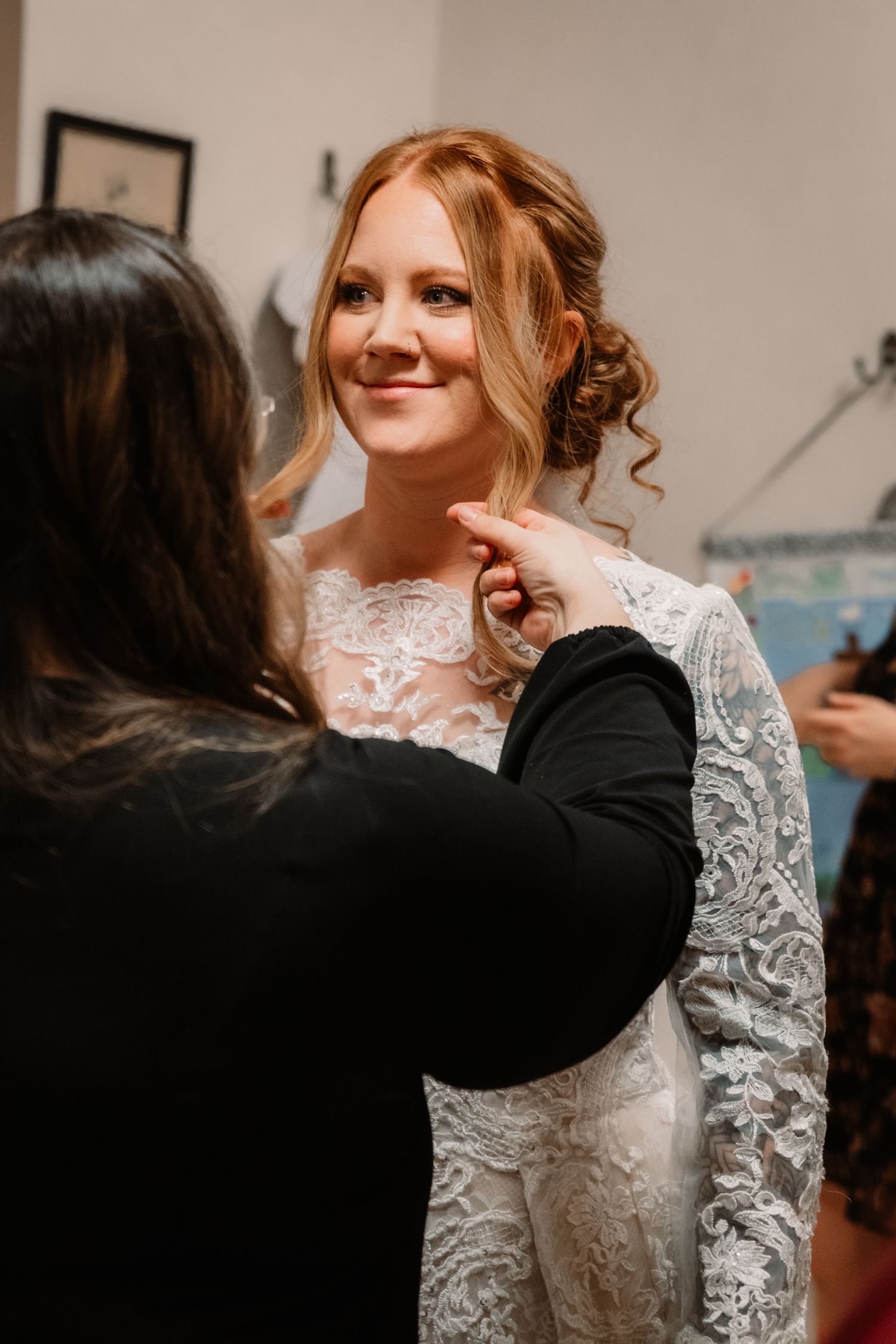 A stylist makes final adjustments to a beautiful lace wedding dress during bridal preparations.