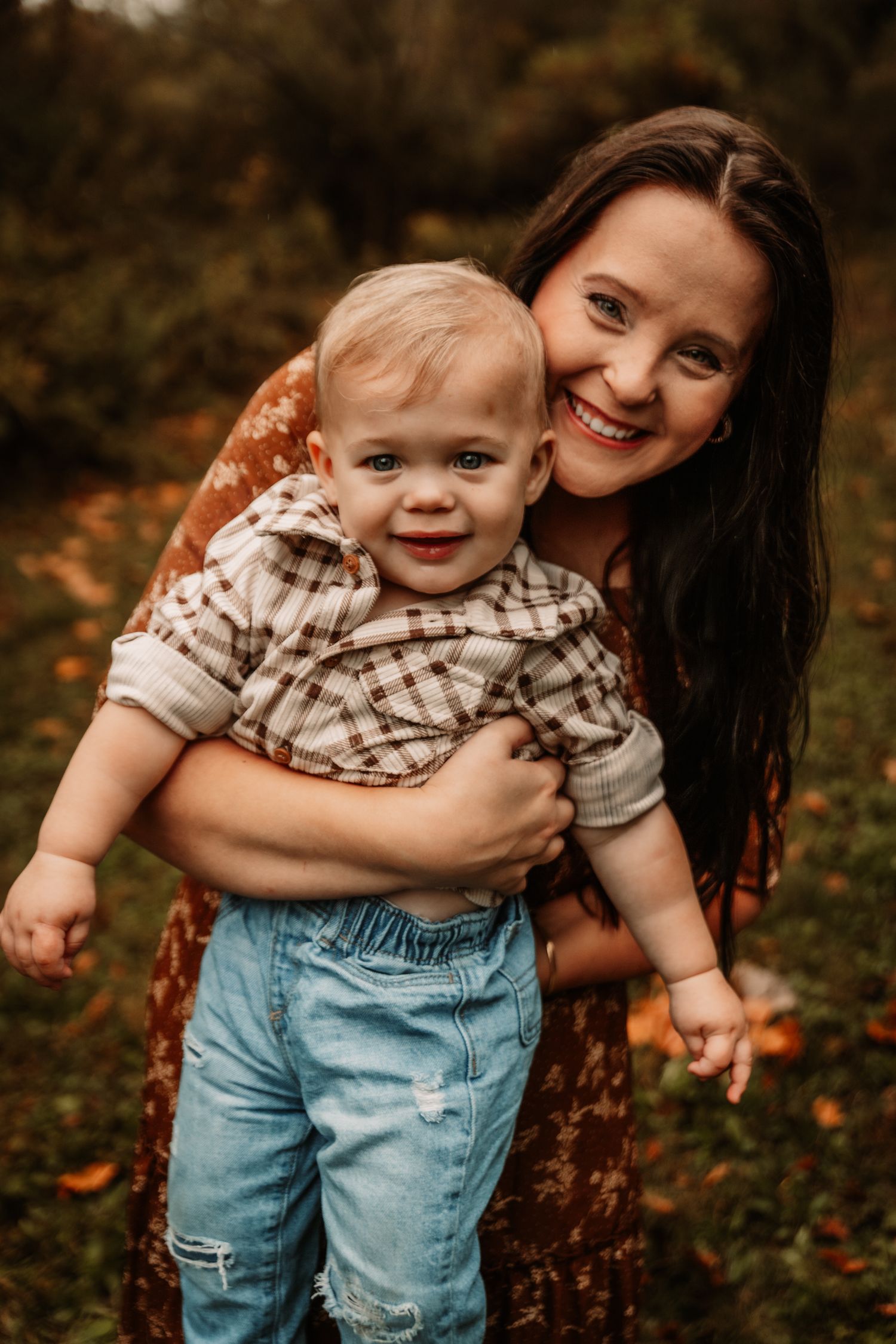A joyful outdoor portrait of a mother and baby against a warm autumn background during golden hour.