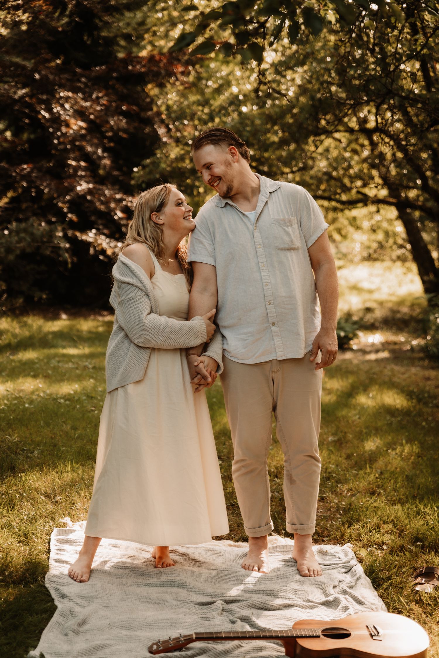 A couple shares a romantic moment on a white blanket in a sun-dappled garden setting with an acoustic guitar nearby.