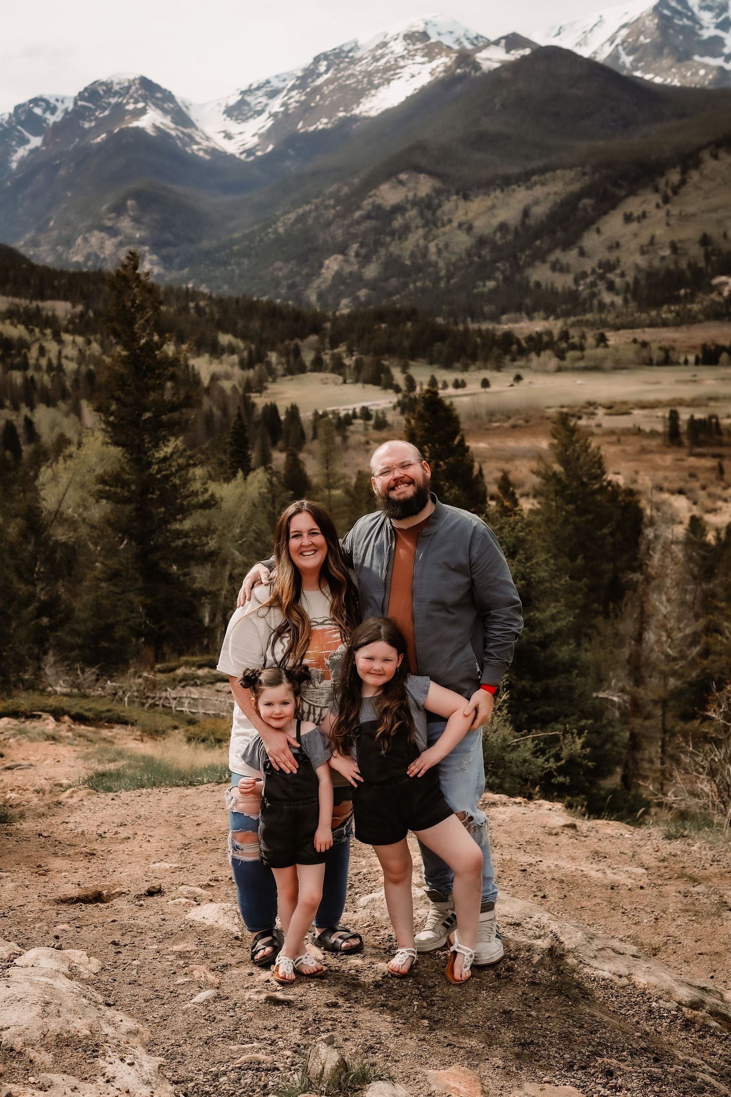 Young family standing on large overlooking valley and view of the mountain in Rocky Mountain National Park by Vine Photo