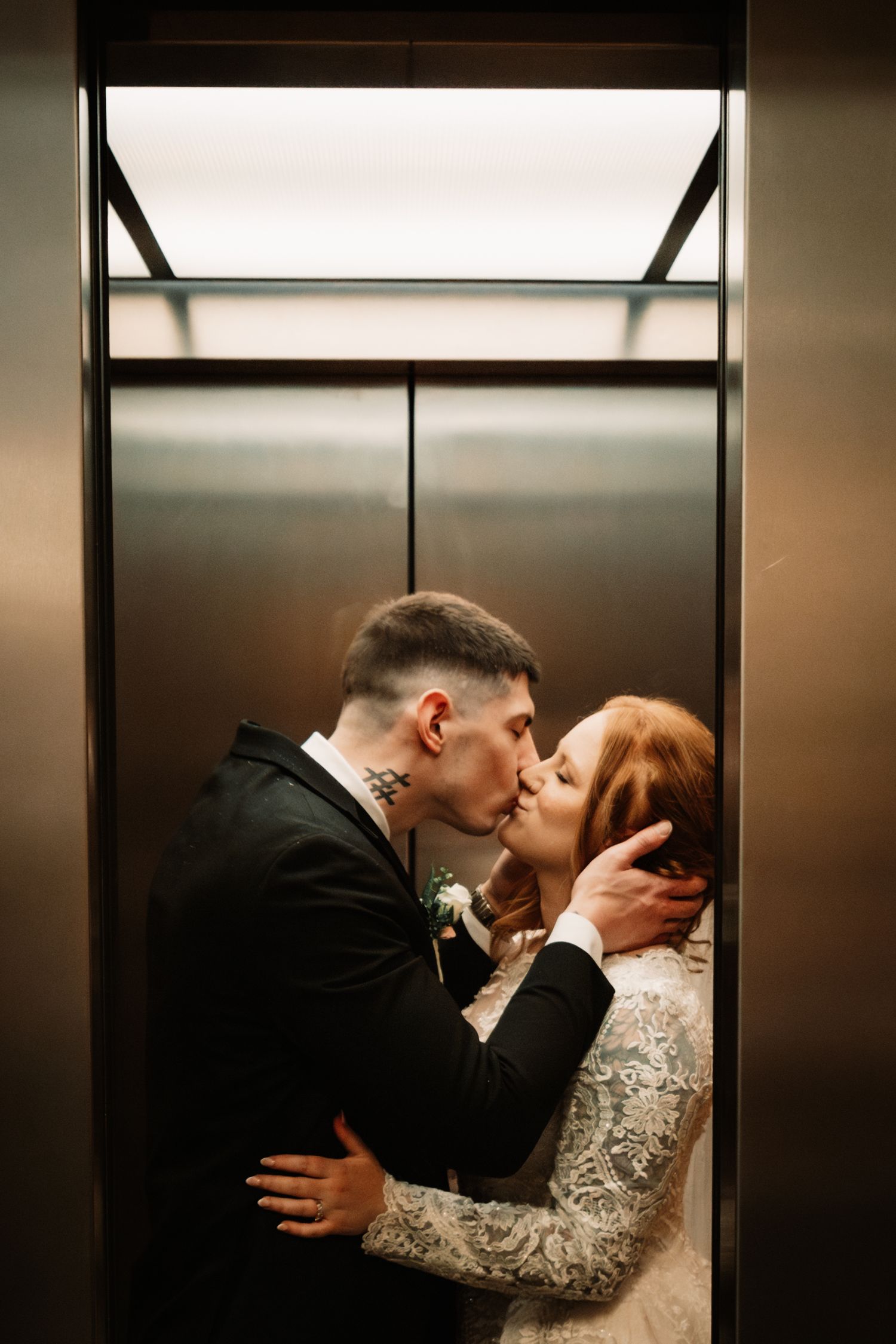 Couple shares an intimate kiss in an elevator while wearing elegant wedding attire.