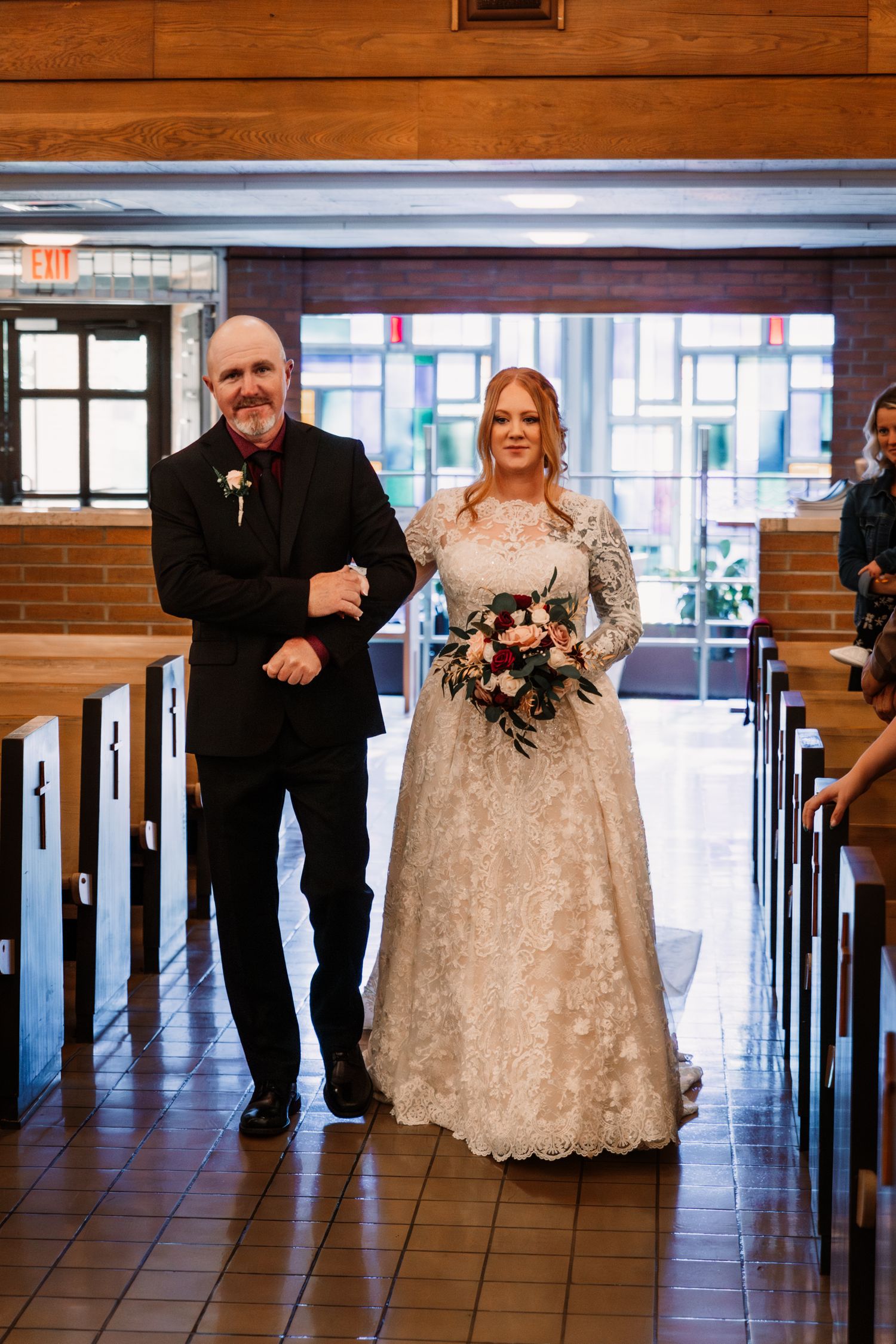 Two people walking down a church aisle with wooden pews and stained glass windows during a wedding ceremony.