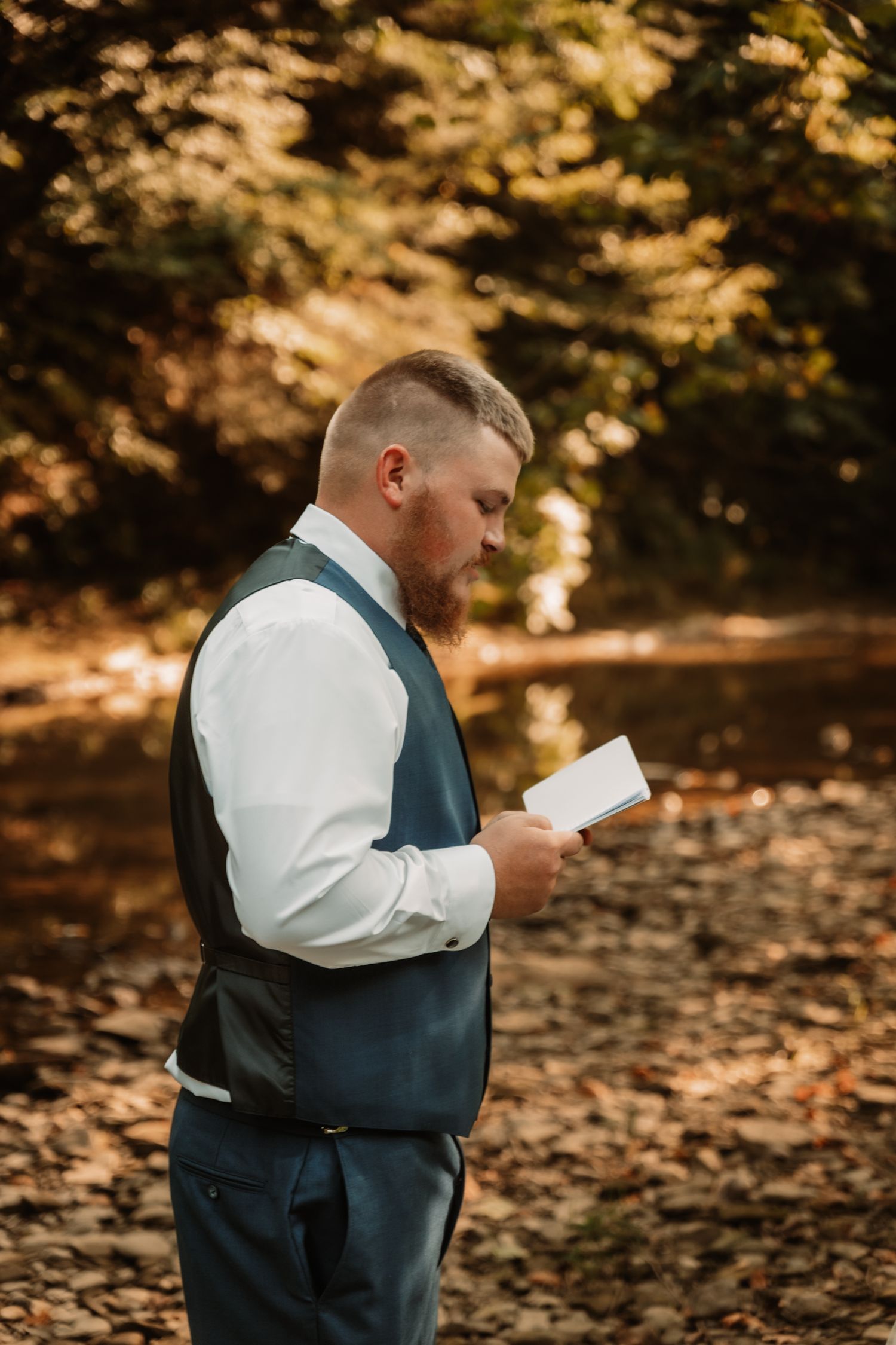A person in a formal vest reads a letter outdoors in an autumn setting with golden light filtering through trees.