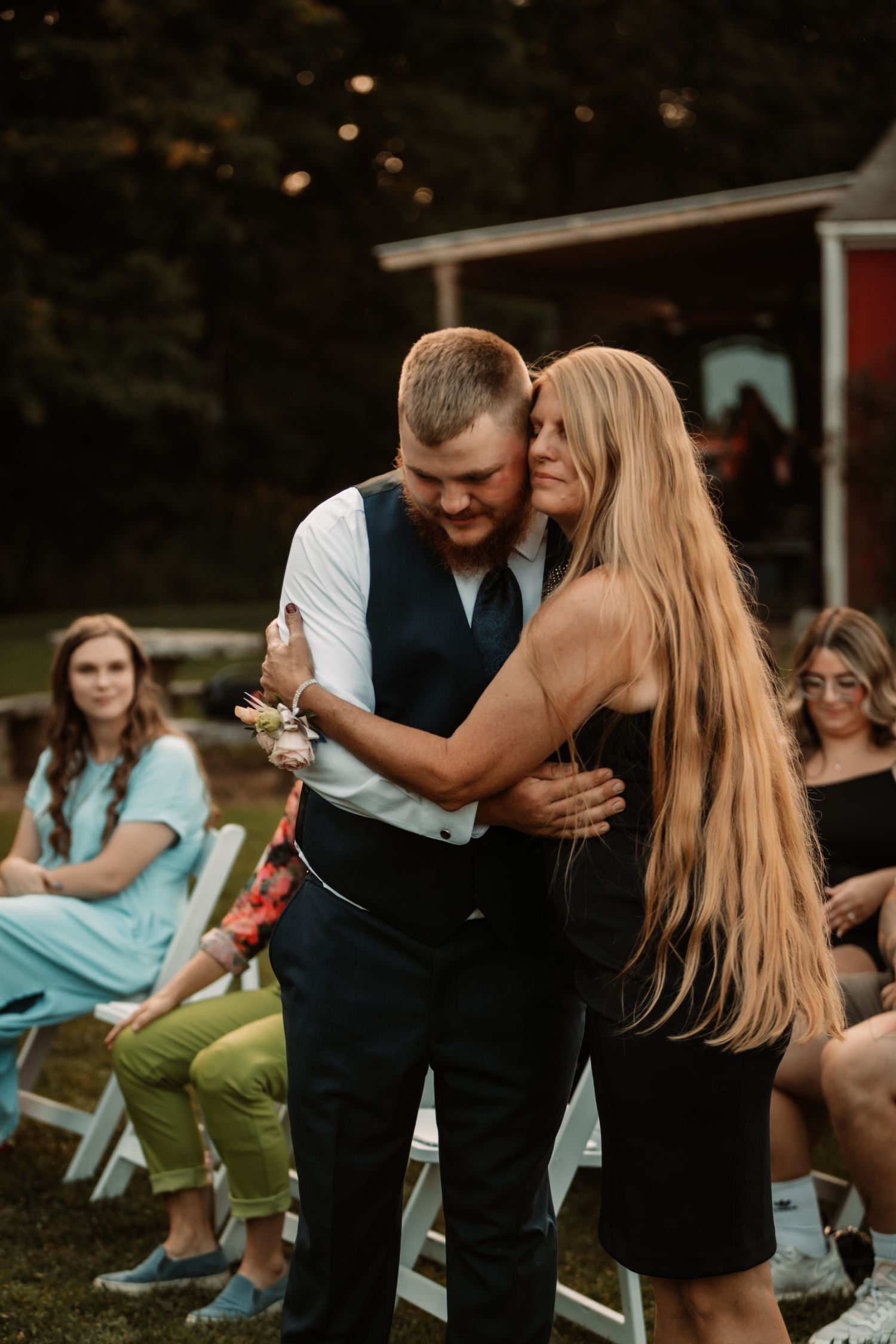 A couple dances together at an outdoor event while guests watch from folding chairs in the background.