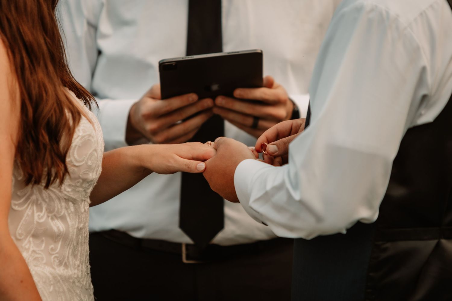 Close-up of hands exchanging rings during a wedding ceremony with a black book in the background.