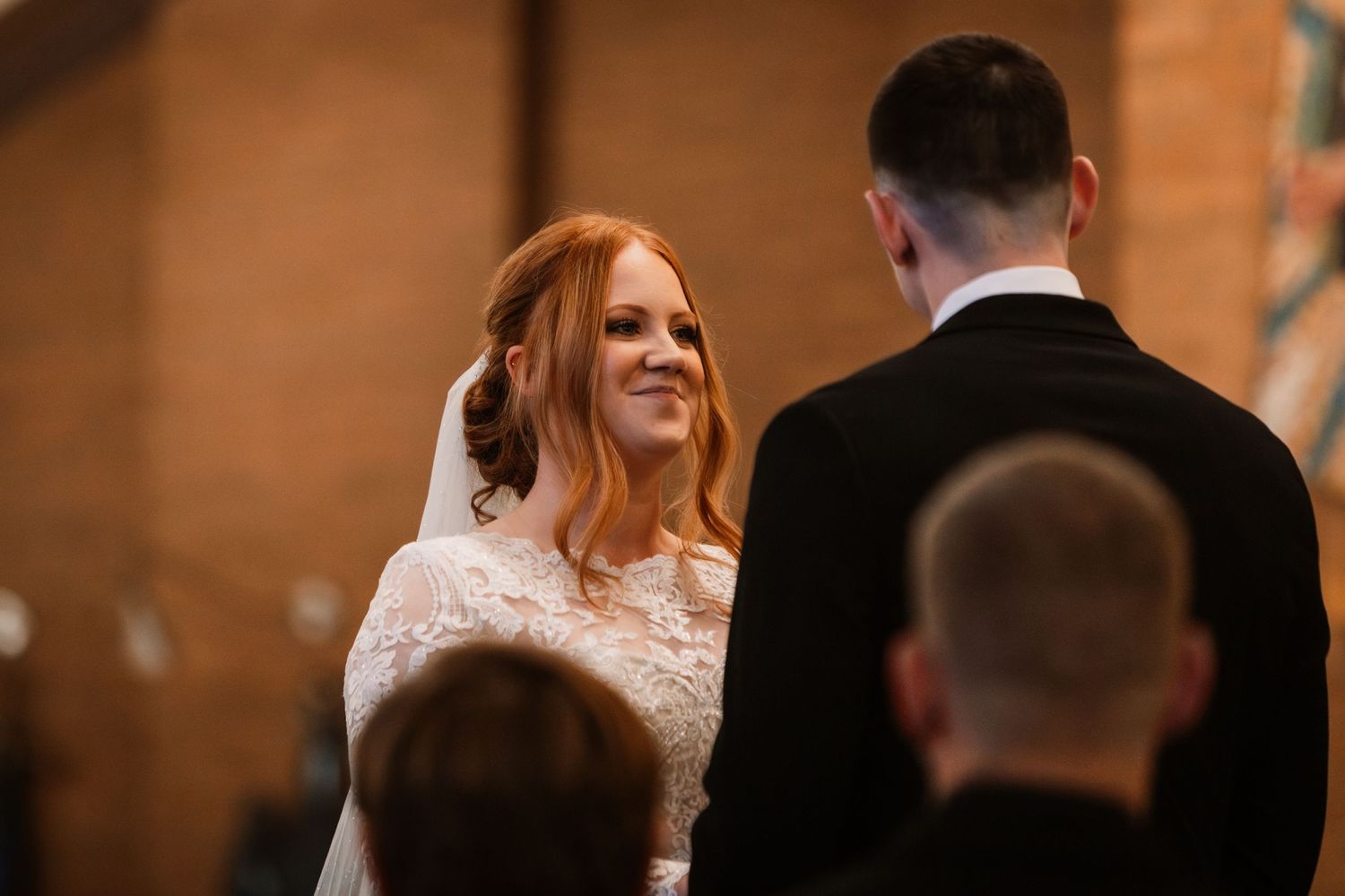 A joyful bride in a lace wedding dress exchanges a heartfelt glance with her groom during their wedding ceremony.