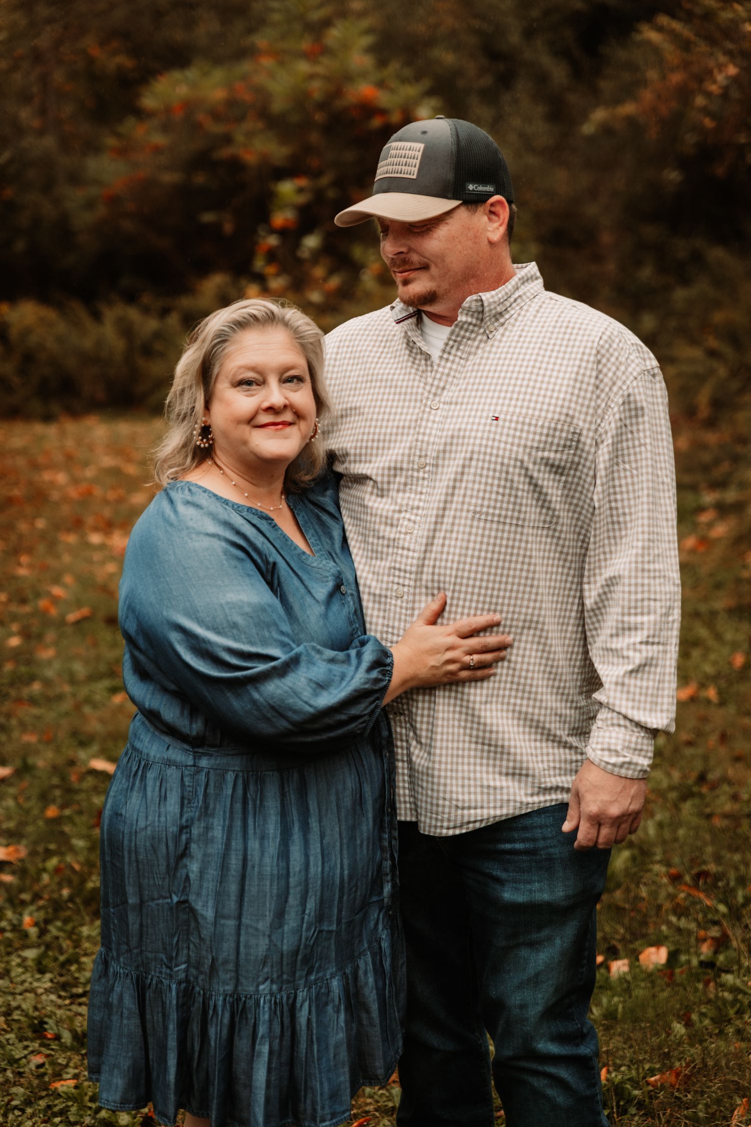 A couple embraces outdoors during an autumn photo session with fall foliage in the background.