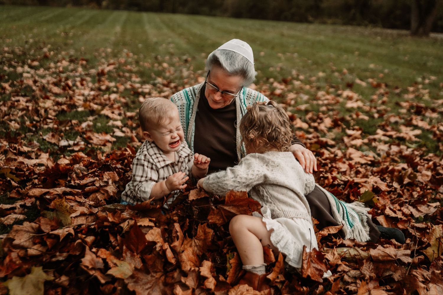 People sit together among fallen autumn leaves on grass during a cozy fall photoshoot.
