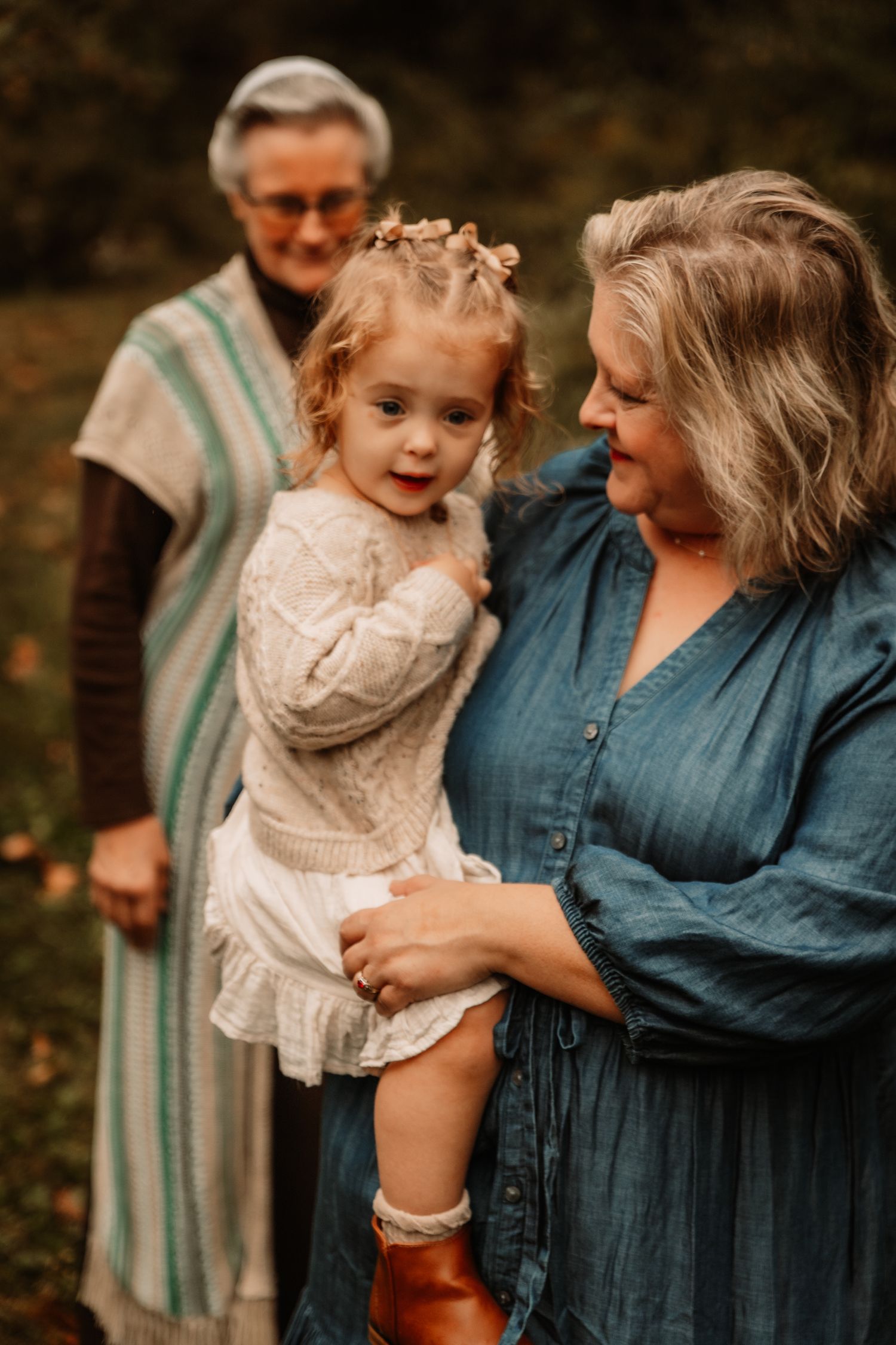 Three generations share a tender outdoor moment in warm autumn lighting, wearing casual clothing and creating a heartwarming scene.