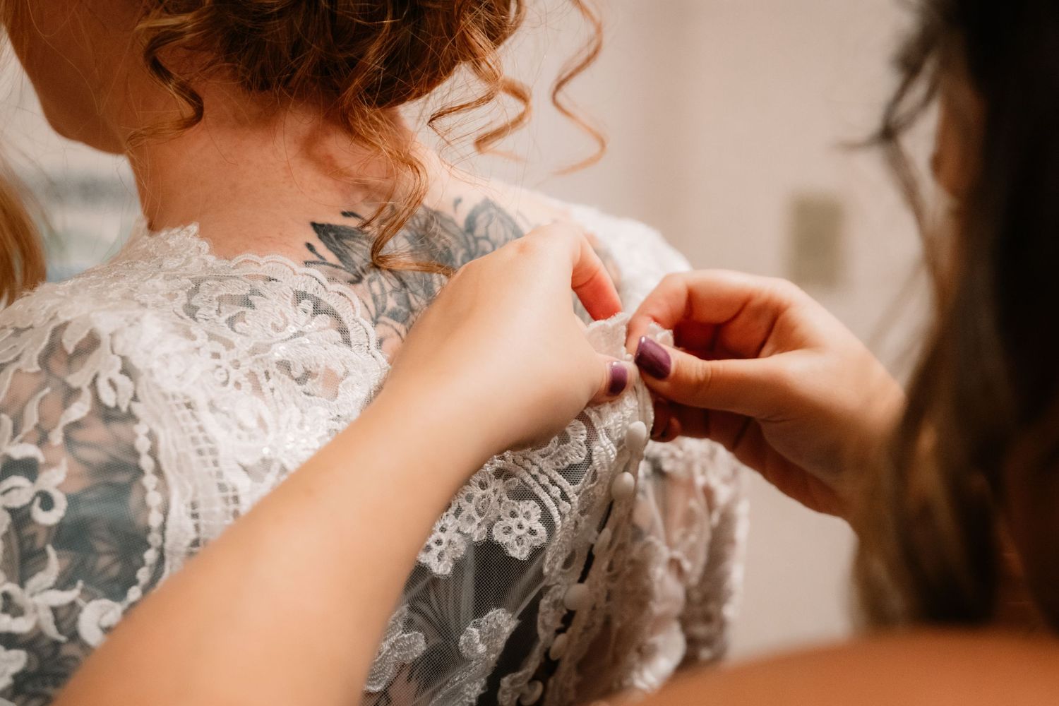 Close up view of someone buttoning a delicate white lace wedding dress with intricate details.