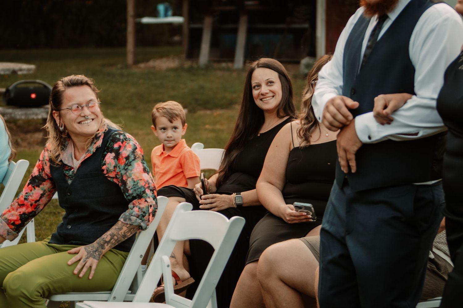 Wedding guests sitting in white chairs at an outdoor ceremony share joyful moments together during the event.