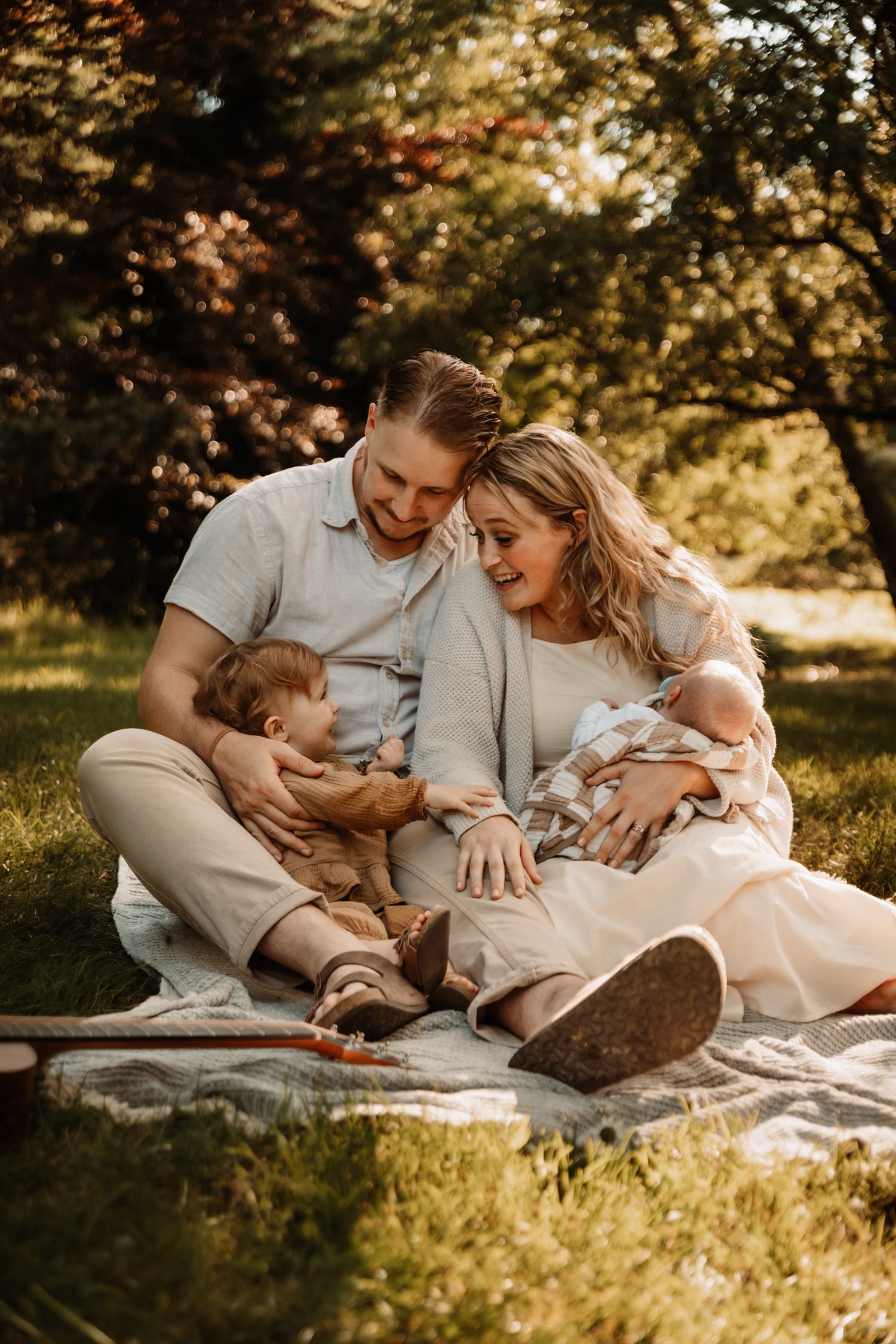 Couple in light colored outfits having a romantic picnic on blanket under autumn trees in warm golden sunlight.