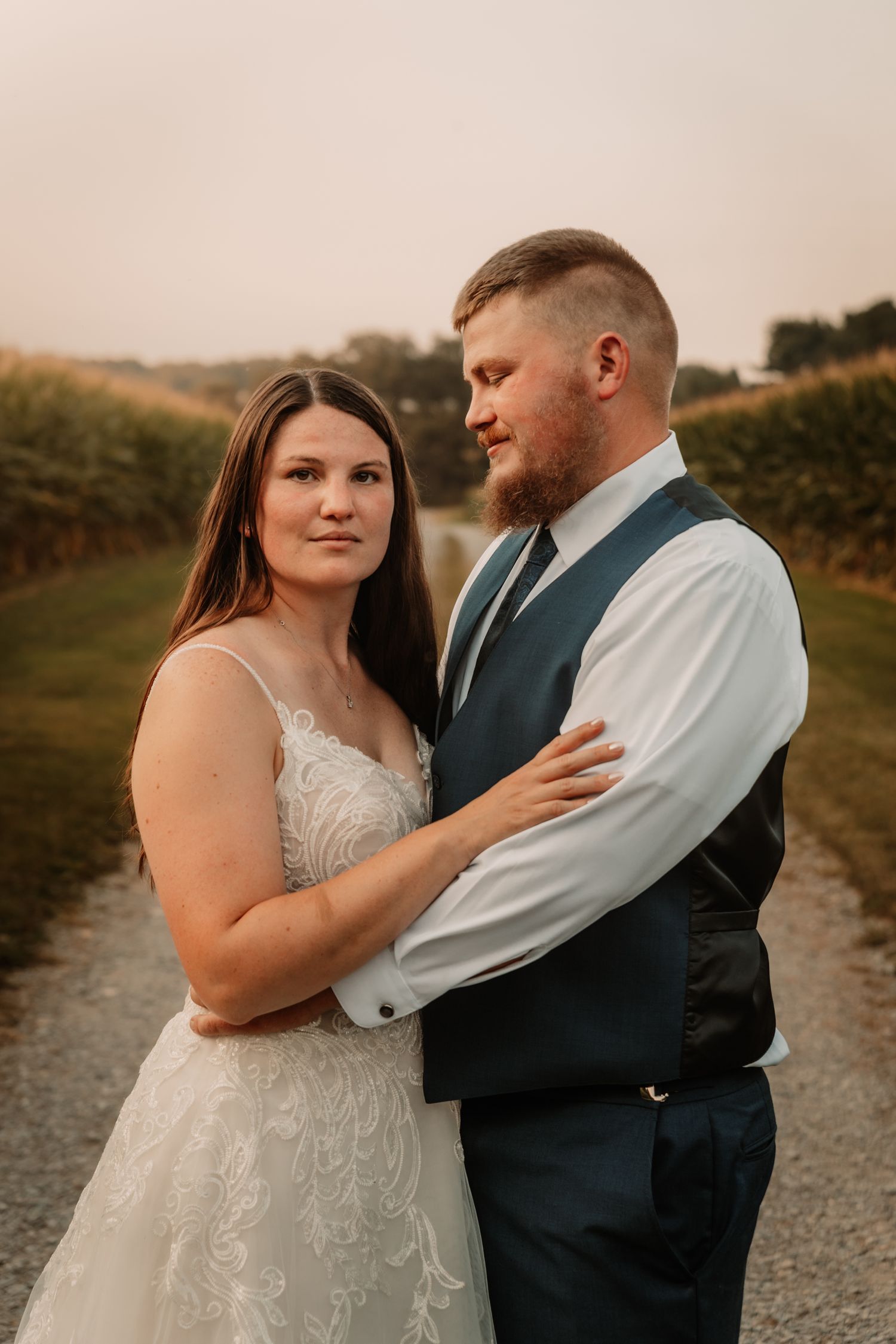 A romantic outdoor wedding photo of a couple embracing on a country path at sunset in warm golden light.
