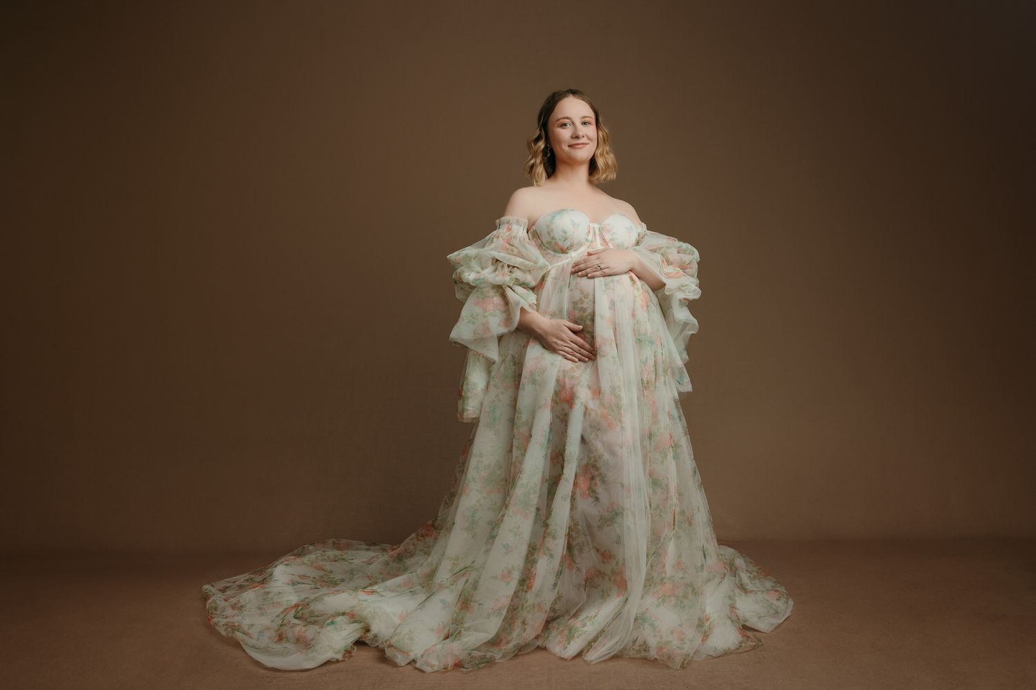 Elegant maternity portrait featuring flowing white lace gown with dramatic train against warm brown studio backdrop in victoria bc studio