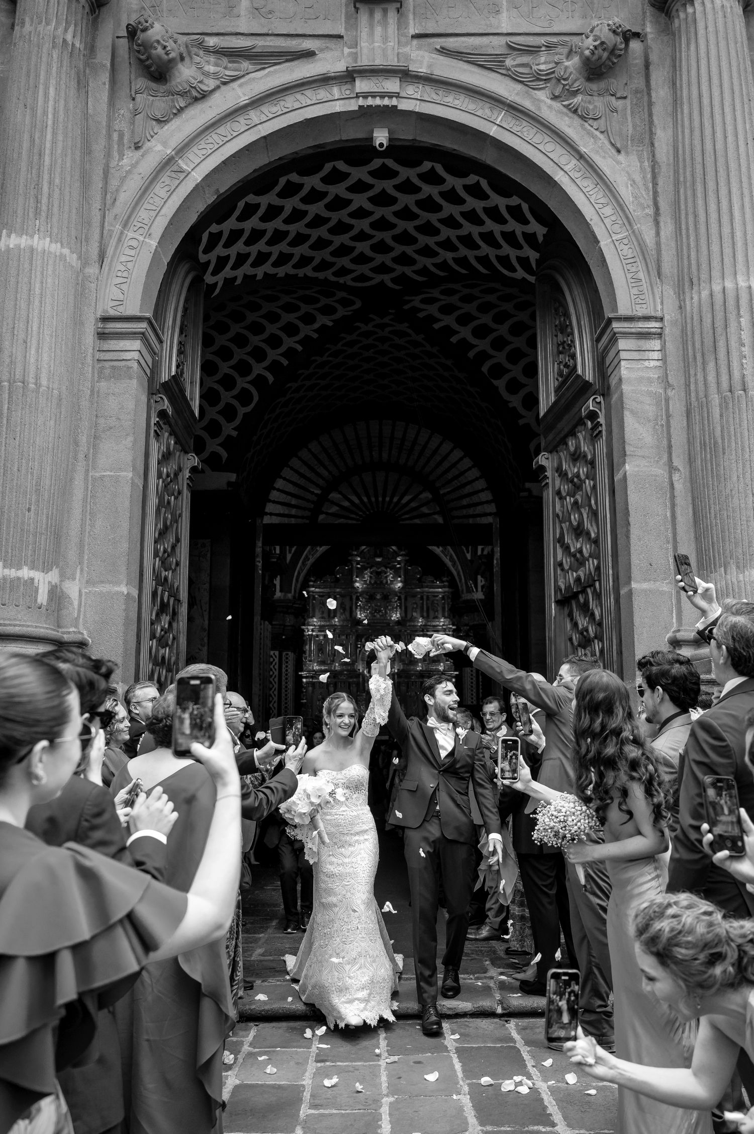 Wedding celebration with flower petals being tossed under an ornate stone archway.