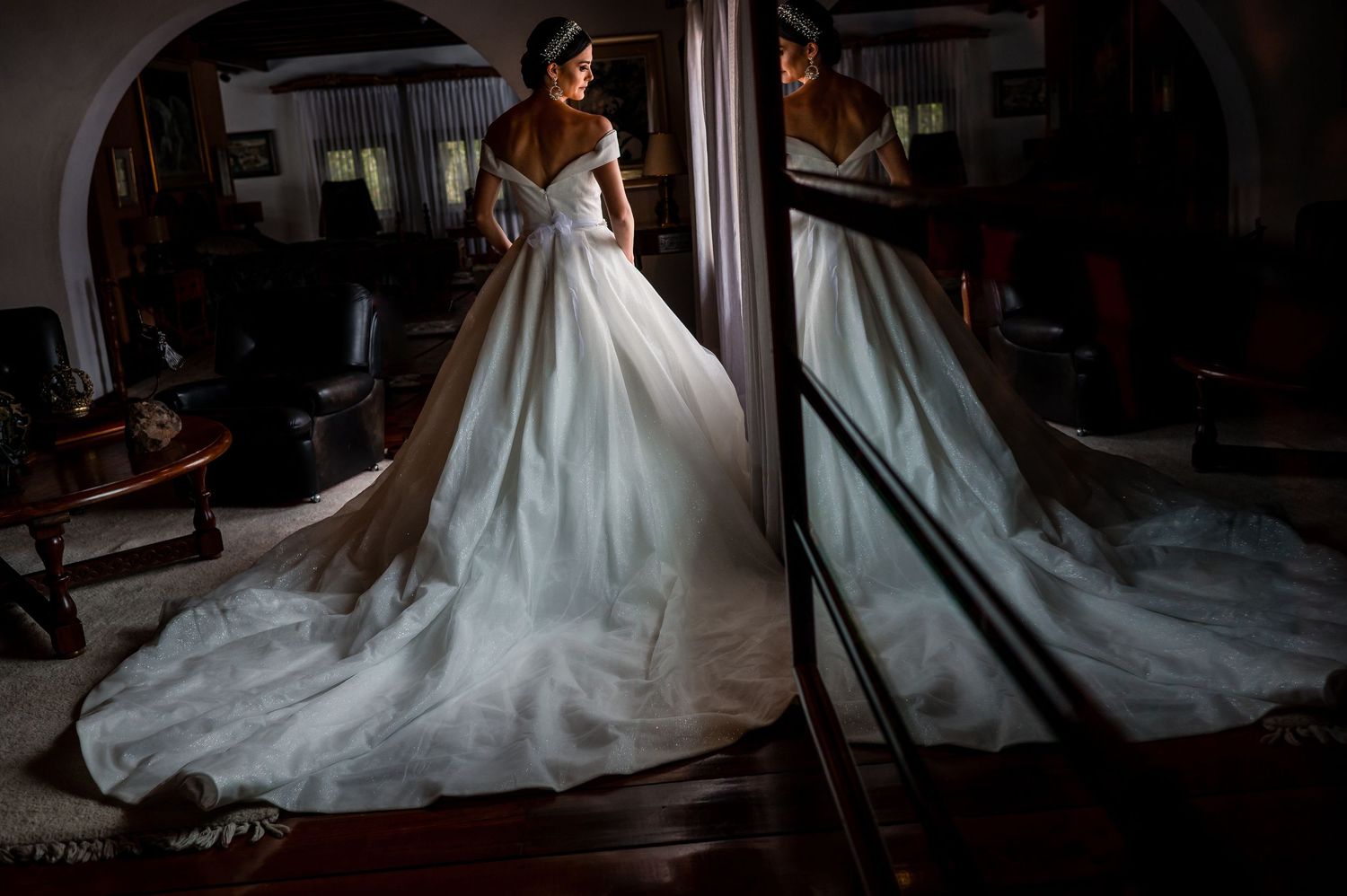 Dramatic silhouette of wedding dress against dark interior setting.