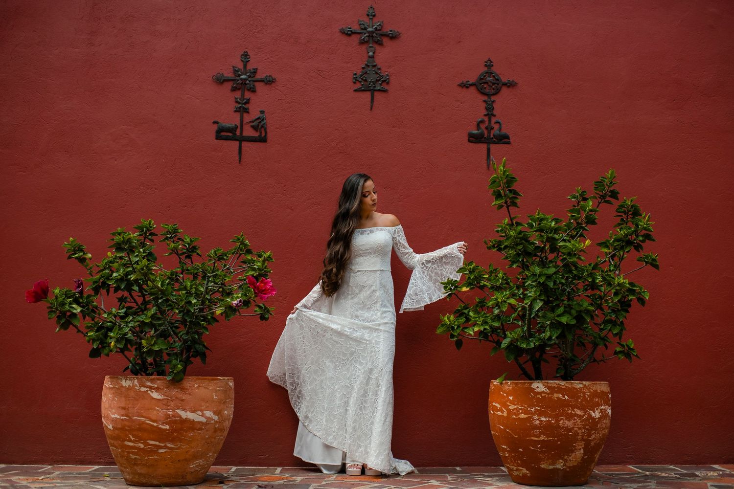 White wedding dress against a red wall with decorative crosses and potted plants.