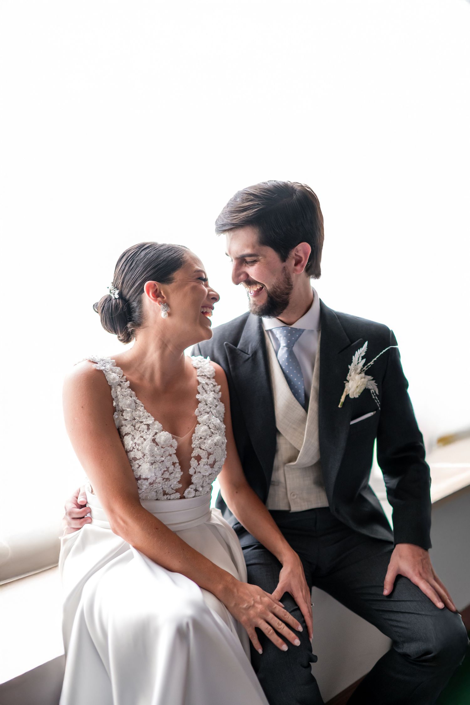 Intimate wedding couple sharing a tender moment while sitting together in a bright window setting.