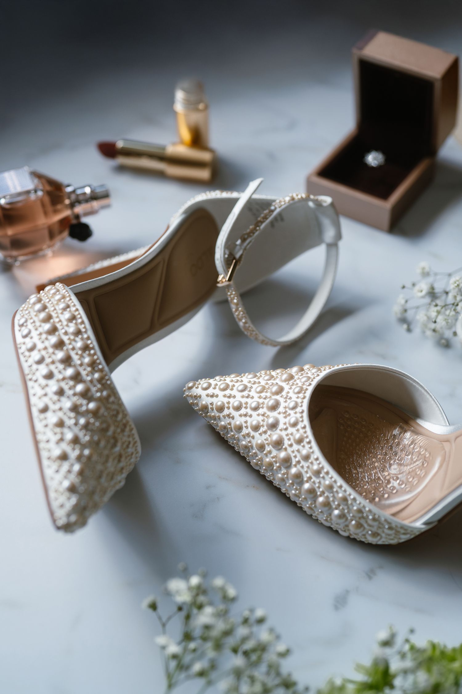 Pearl-embellished bridal shoes photographed with delicate details on marble surface.
