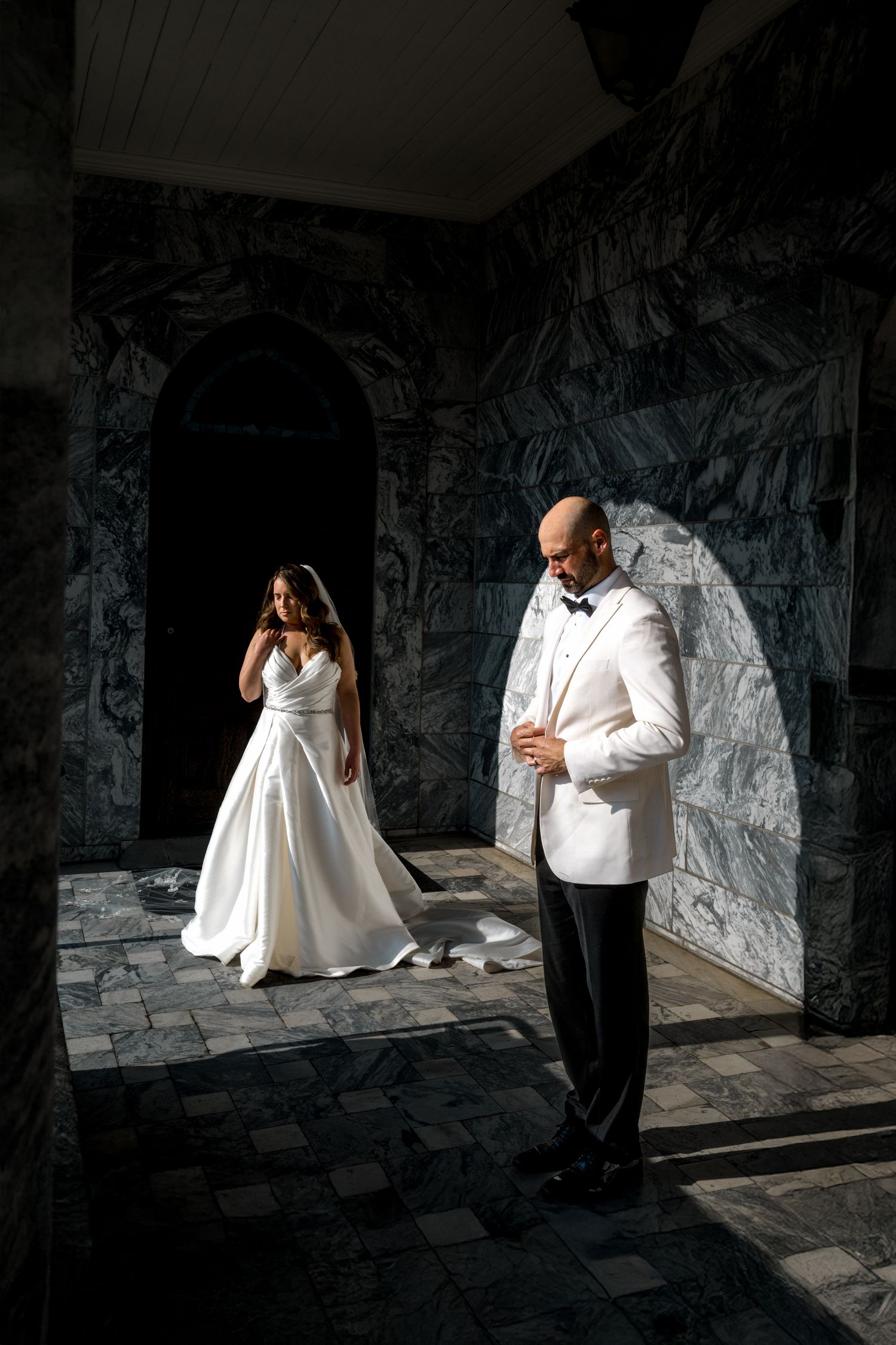 Artistic wedding photos in a stone corridor with dramatic lighting and shadows.