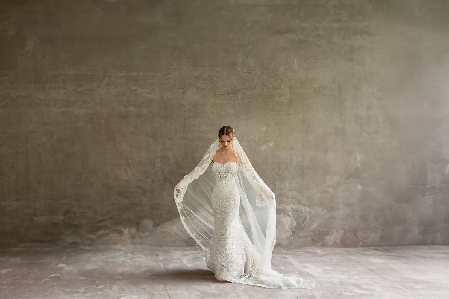 Artistic bridal portraits in white against a textured grey background showing flowing movement.