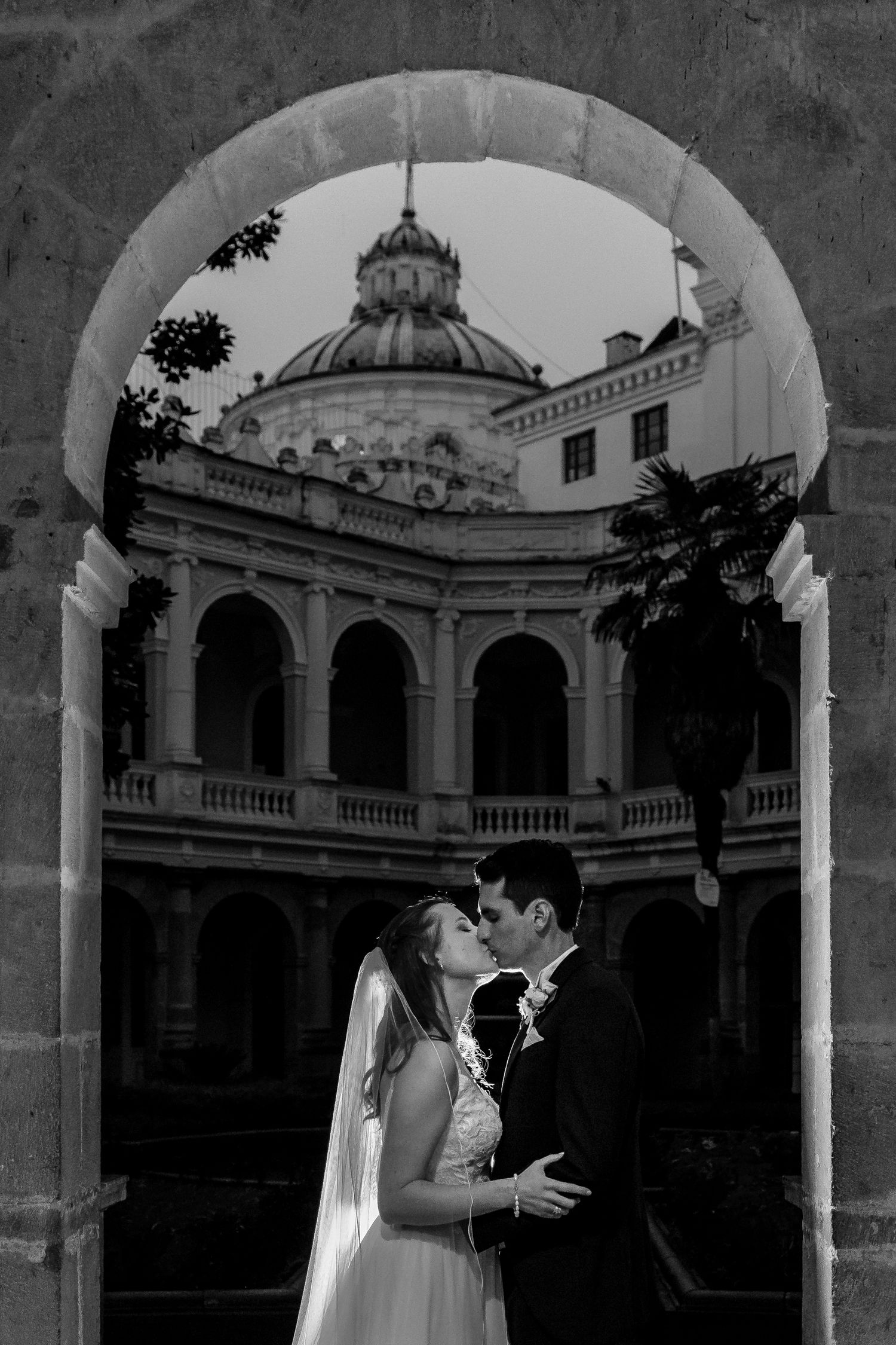 Romantic wedding photo under classical stone archways with ornate architectural details.
