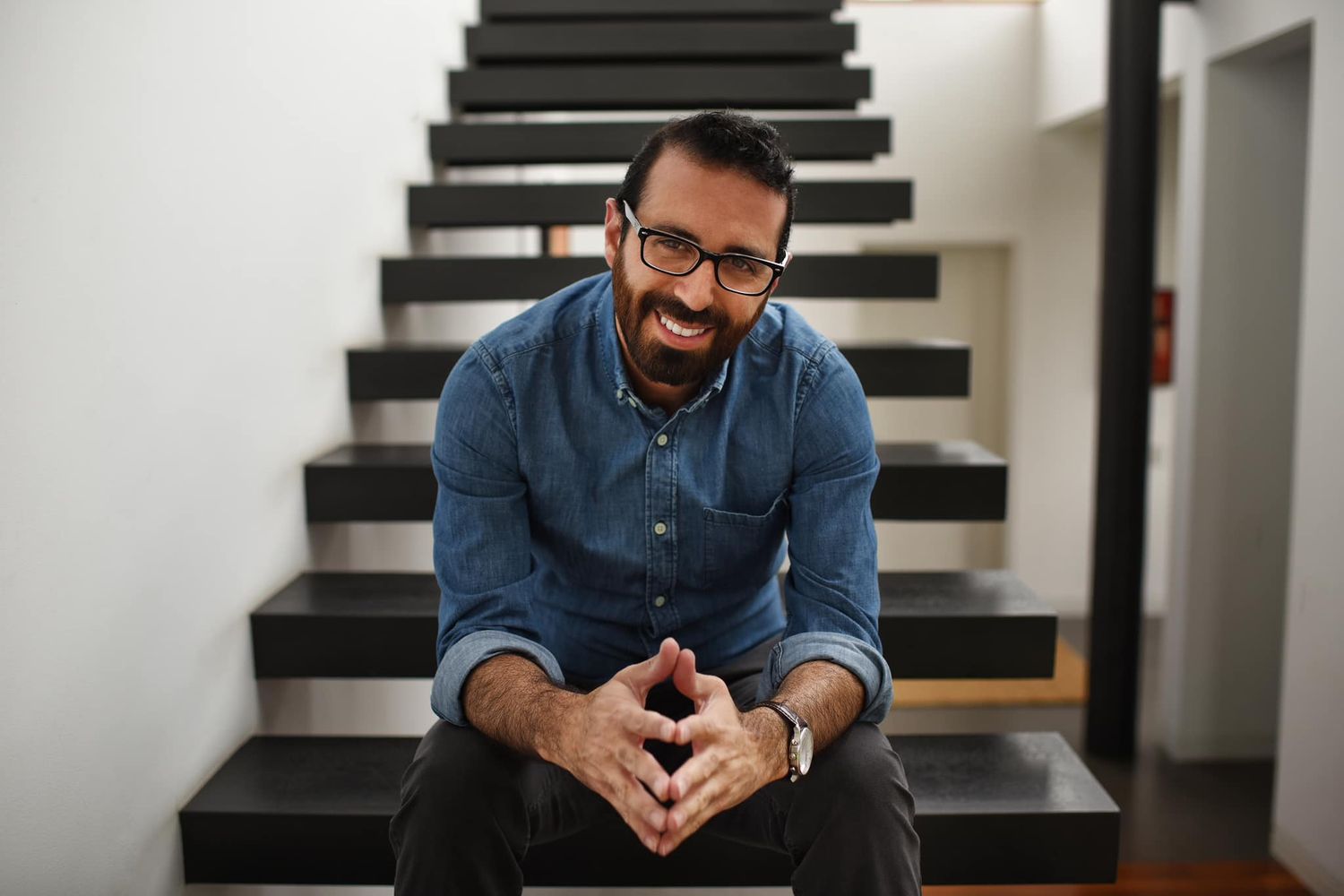 Professional portrait of person sitting on modern black staircase.