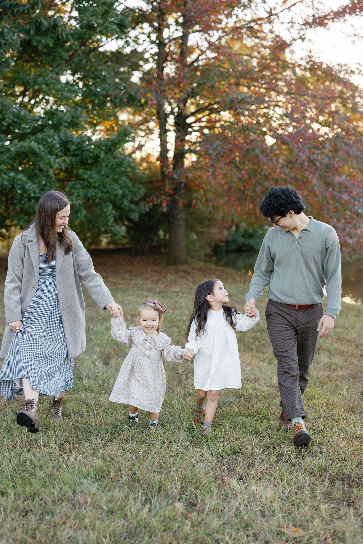 A family walks together through an autumn field with golden sunlight filtering through fall foliage in the background.