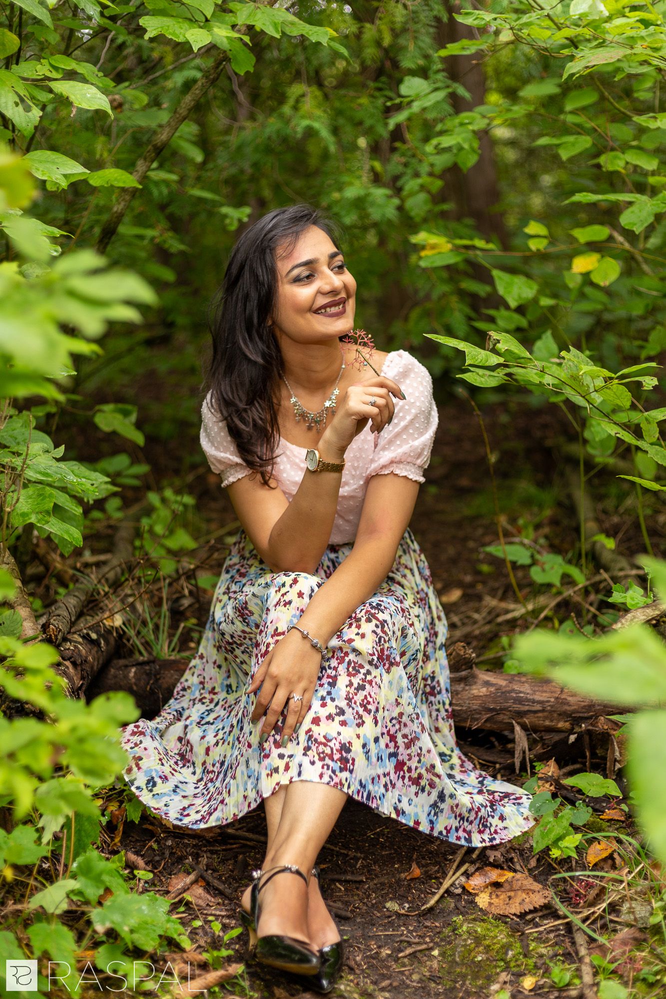 A floral dress and white top create a summery look against lush green foliage in a natural outdoor setting.