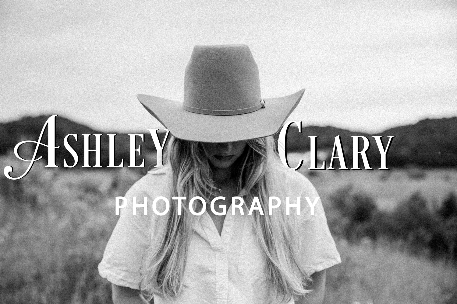 Black and white photo of a woman in a wide-brim hat and white shirt with long hair in a field, Ashley Clary Photography logo.