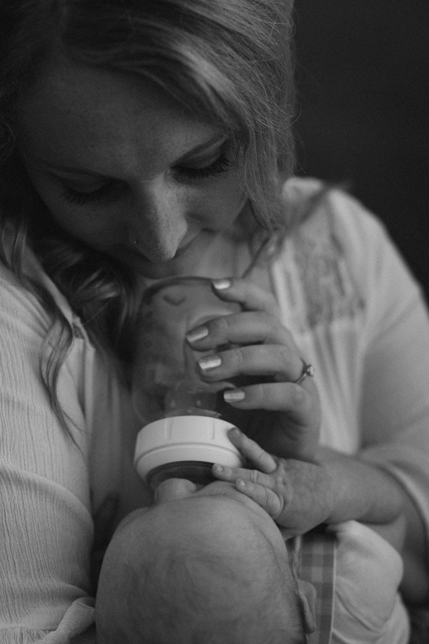 Black and white photo of a mother tenderly kissing her newborn baby's head while cradling the infant.