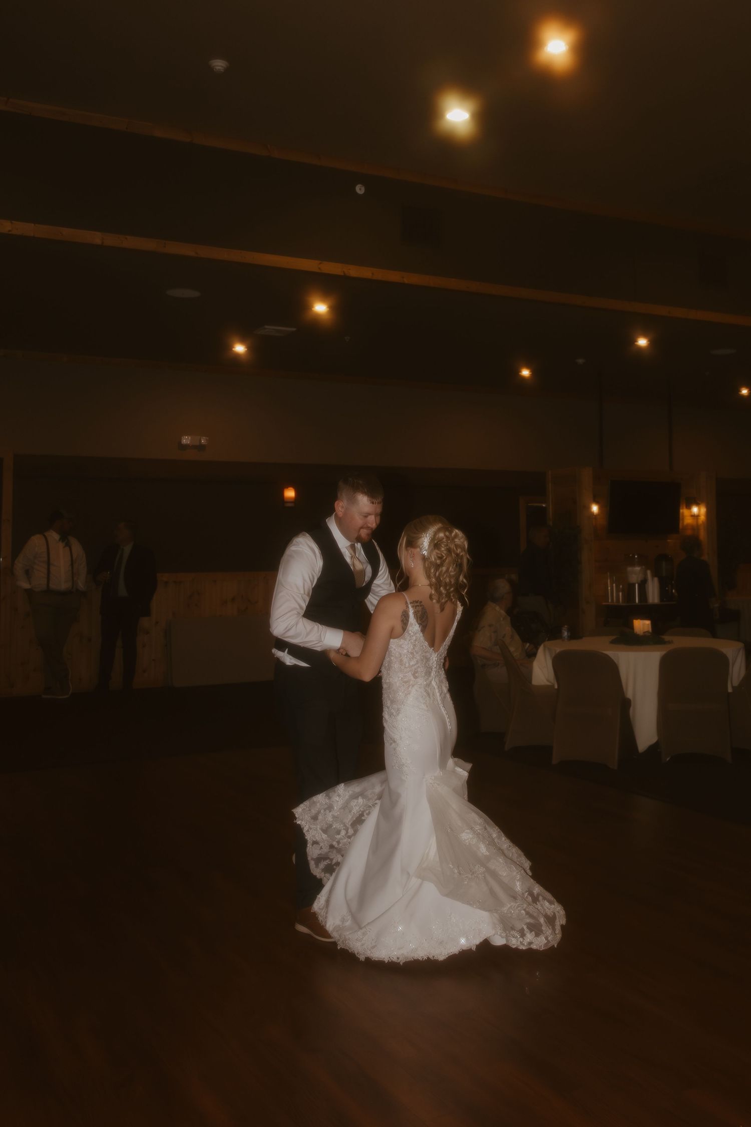 Bride and groom share romantic first dance in dimly lit wedding reception venue.