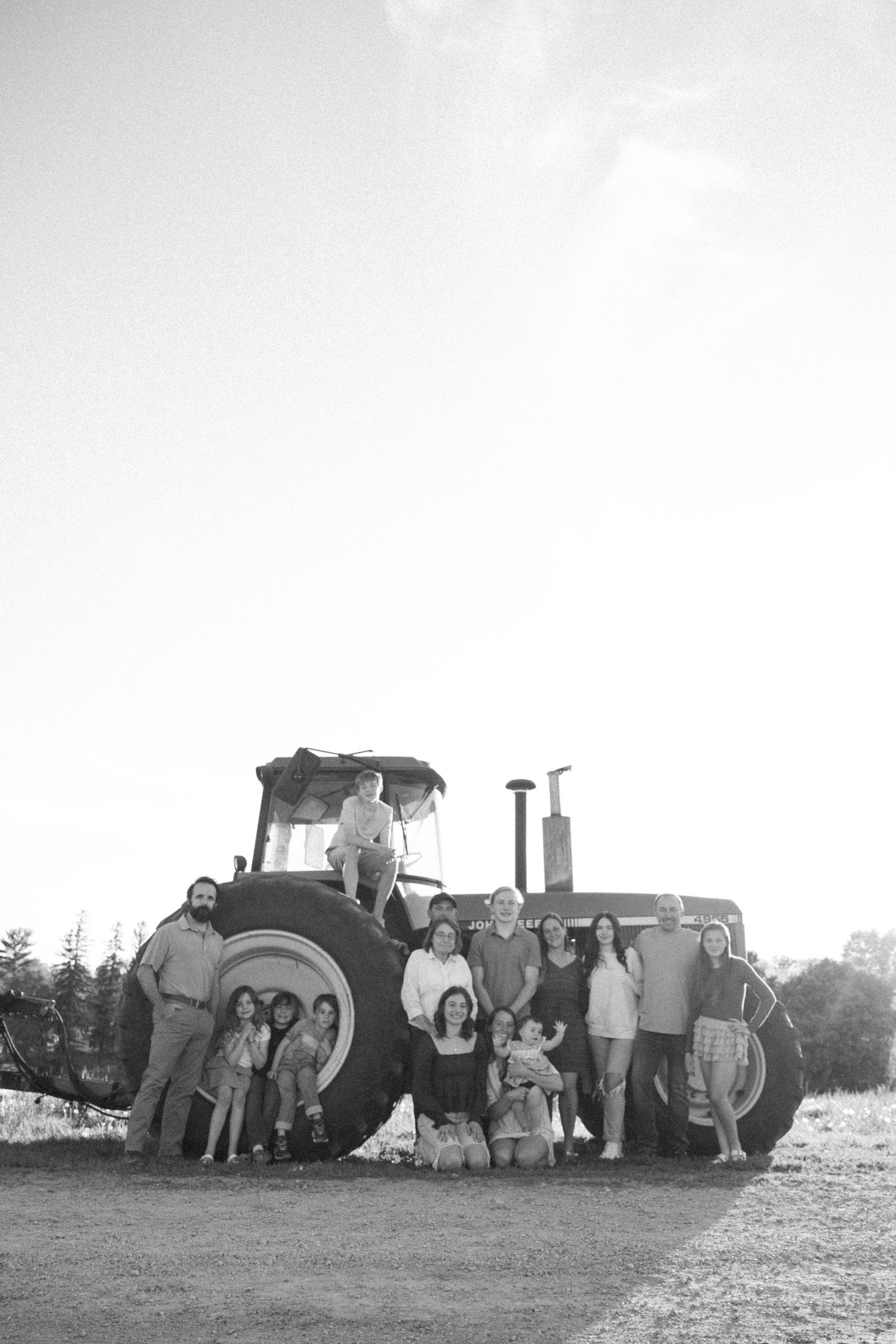 Black and white family photo with large group posing around a vintage tractor on a rural farm.