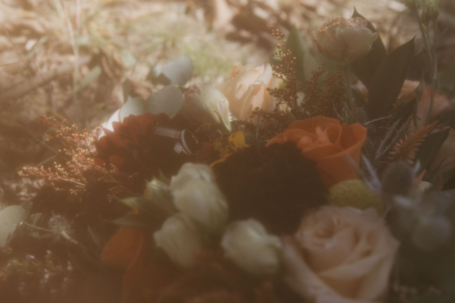 Close-up of an elegant wedding bouquet featuring orange, white, and dark red roses with soft bokeh lighting.