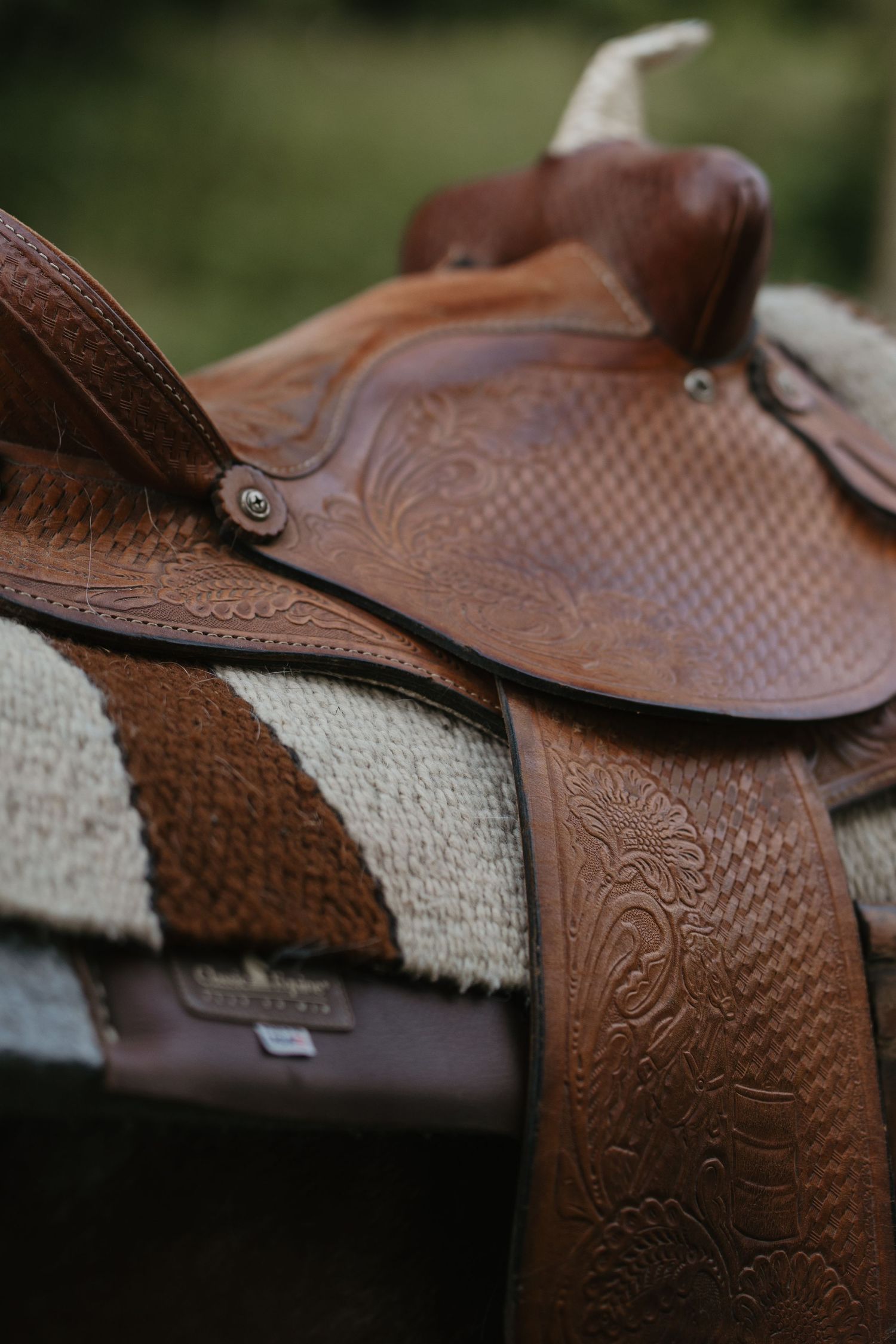 Close-up of an intricately tooled brown leather western saddle with floral patterns resting on a striped blanket.