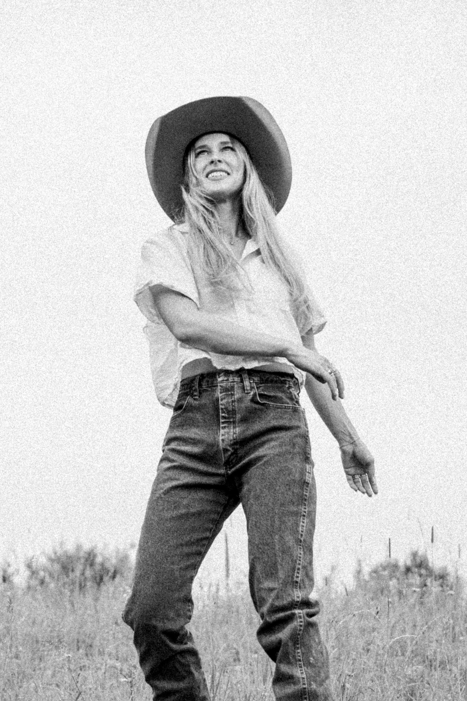 Black and white portrait of someone in western wear posing playfully in a field.