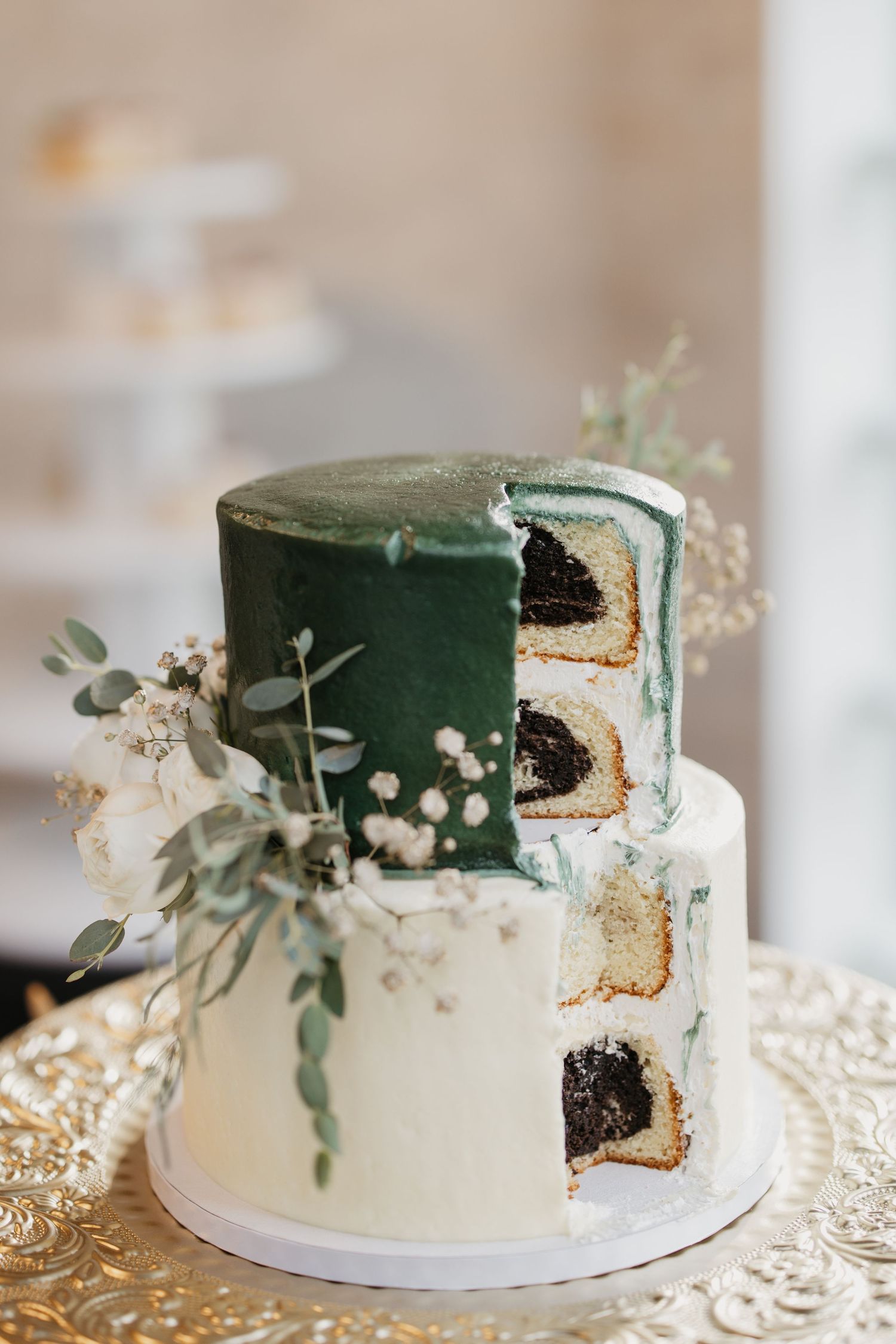 Two-tier wedding cake with emerald green top tier and white base, decorated with eucalyptus and baby's breath, with slices cut out.