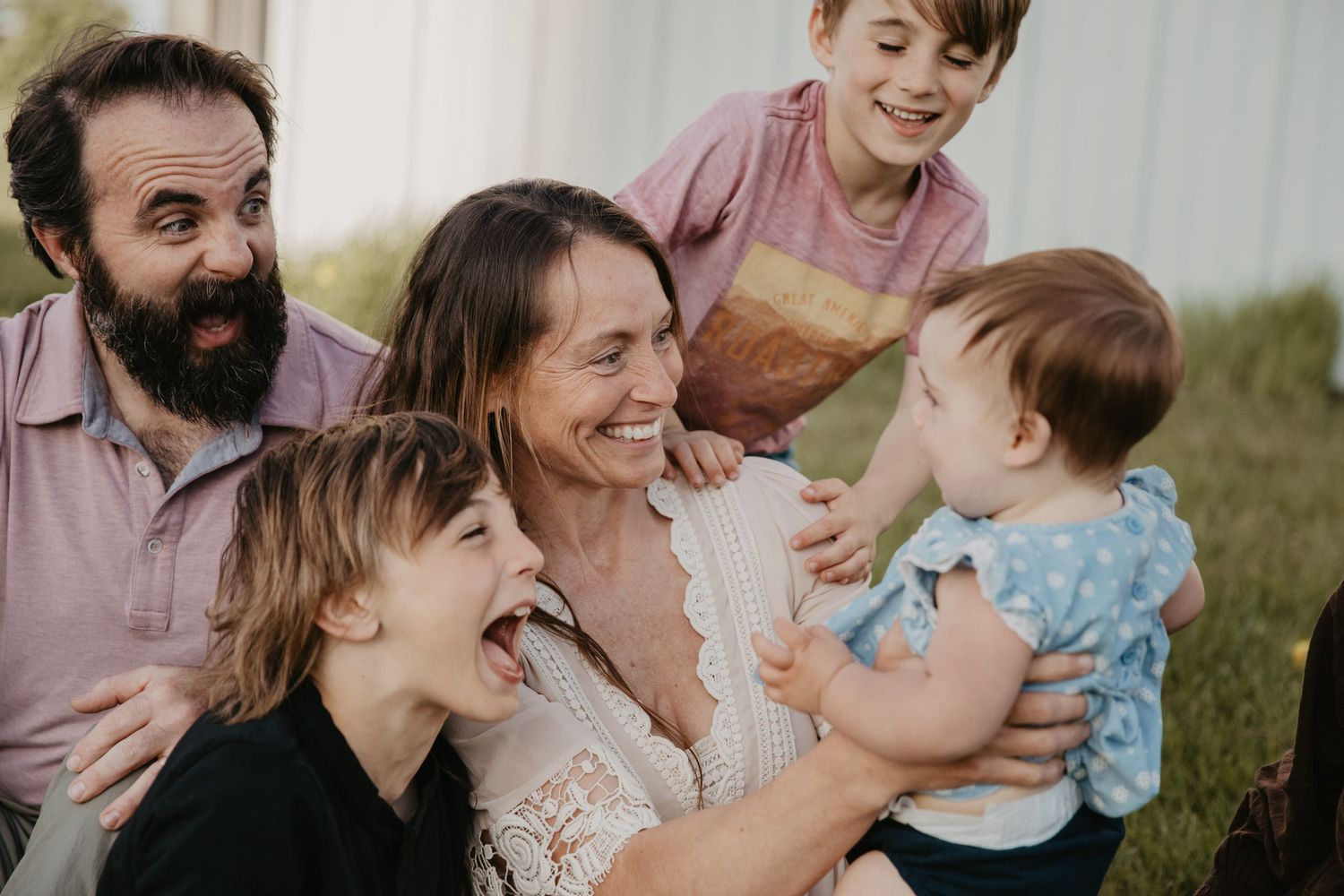 Happy family with parents and three children laughing and bonding together outdoors on a sunny day.