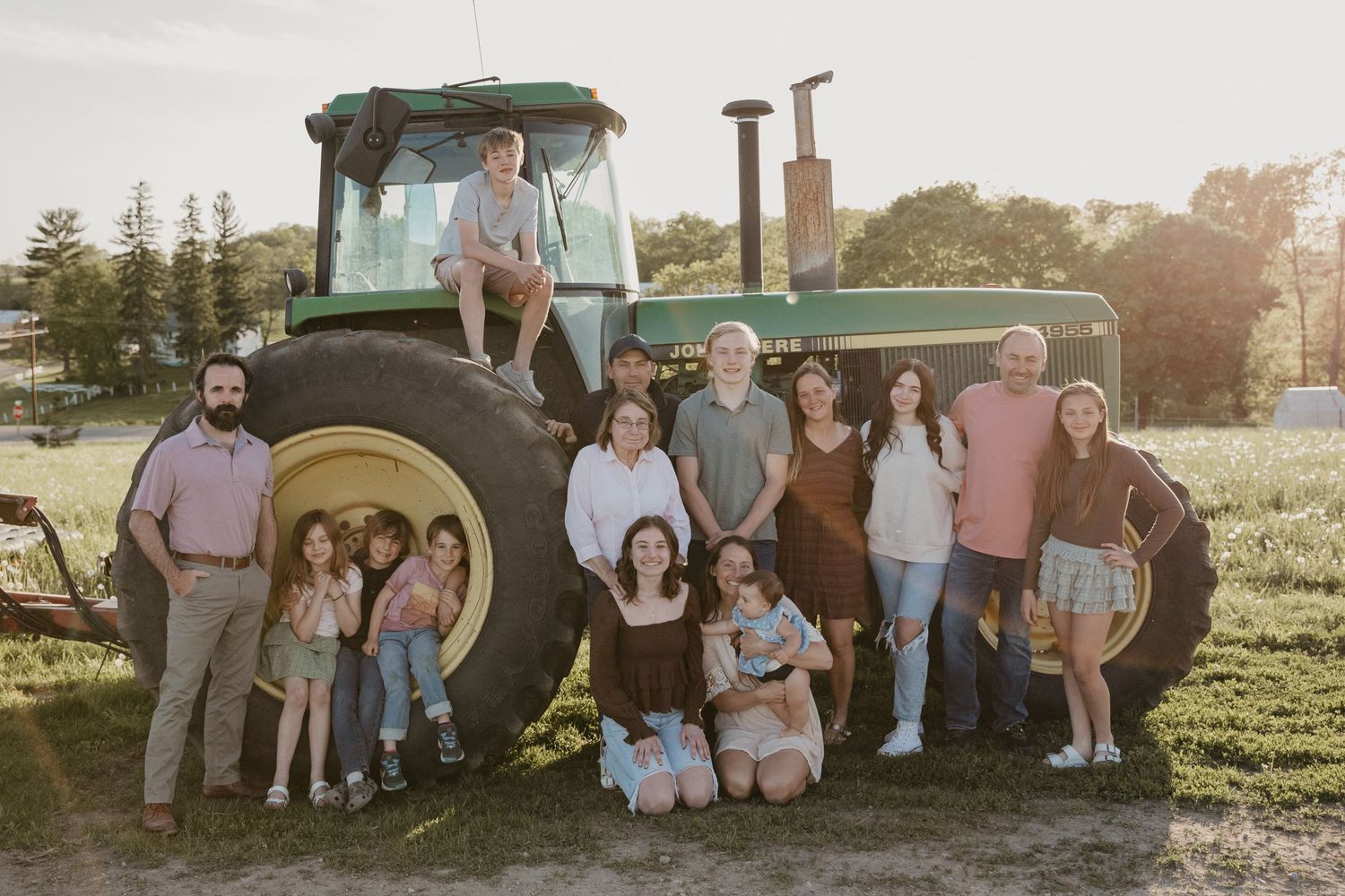 Large family posing together in front of a green John Deere tractor on a farm at golden hour.