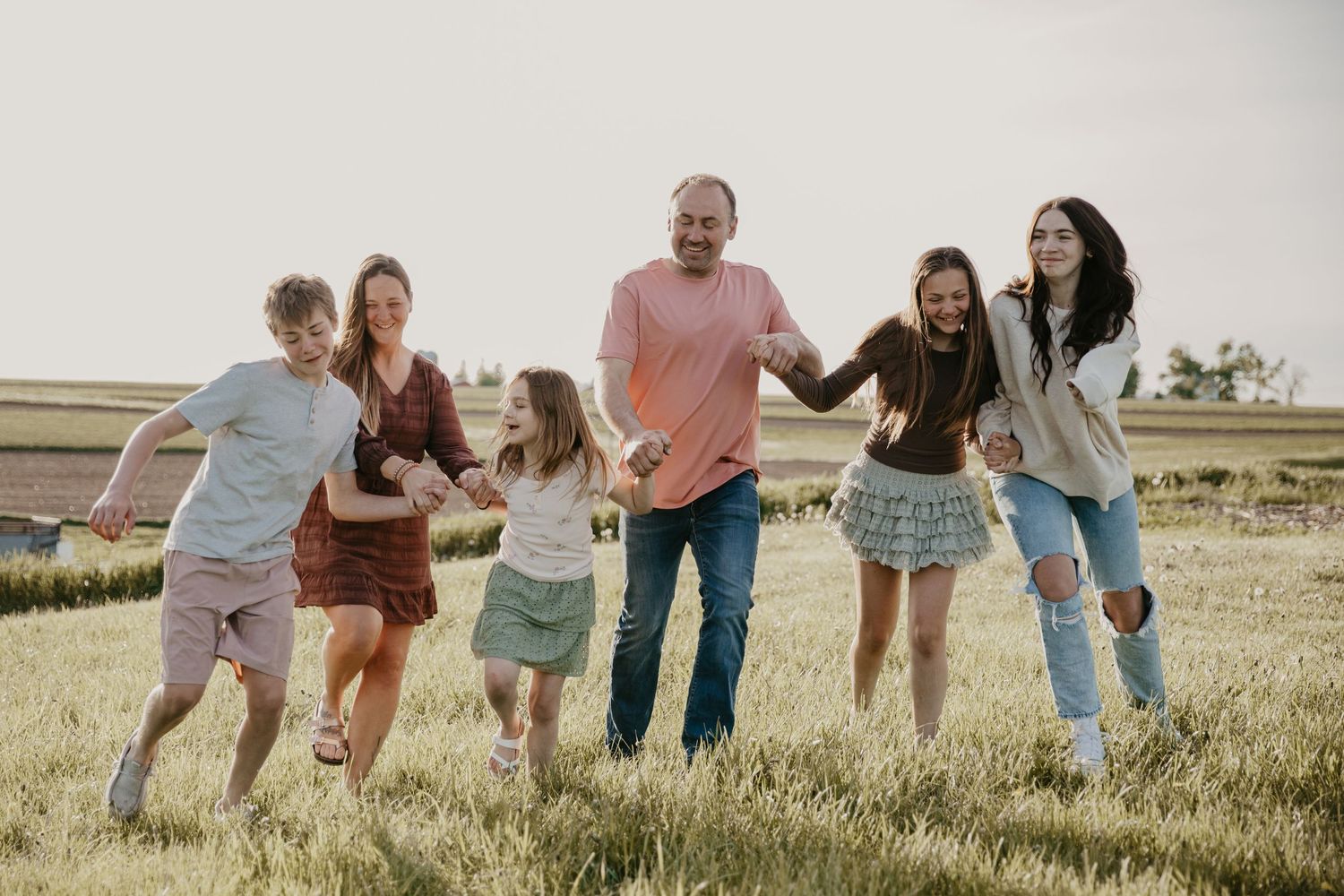 Happy family of six holding hands and running together in a sunny green field during a warm summer day.