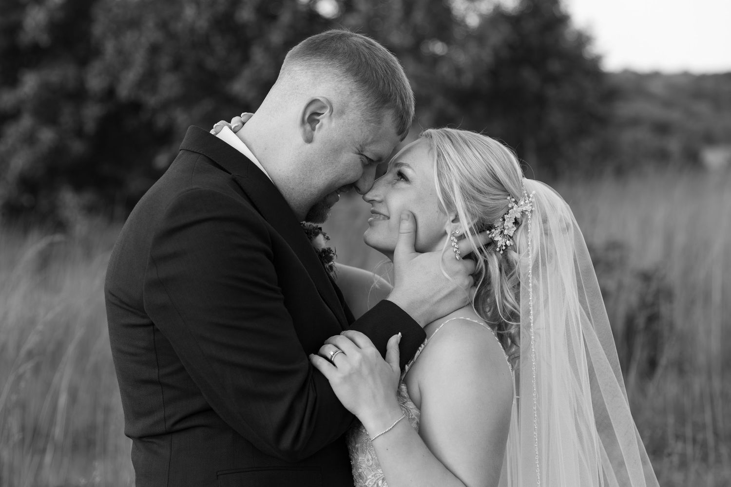 Black and white photo of a bride and groom sharing an intimate forehead touch moment outdoors on their wedding day.