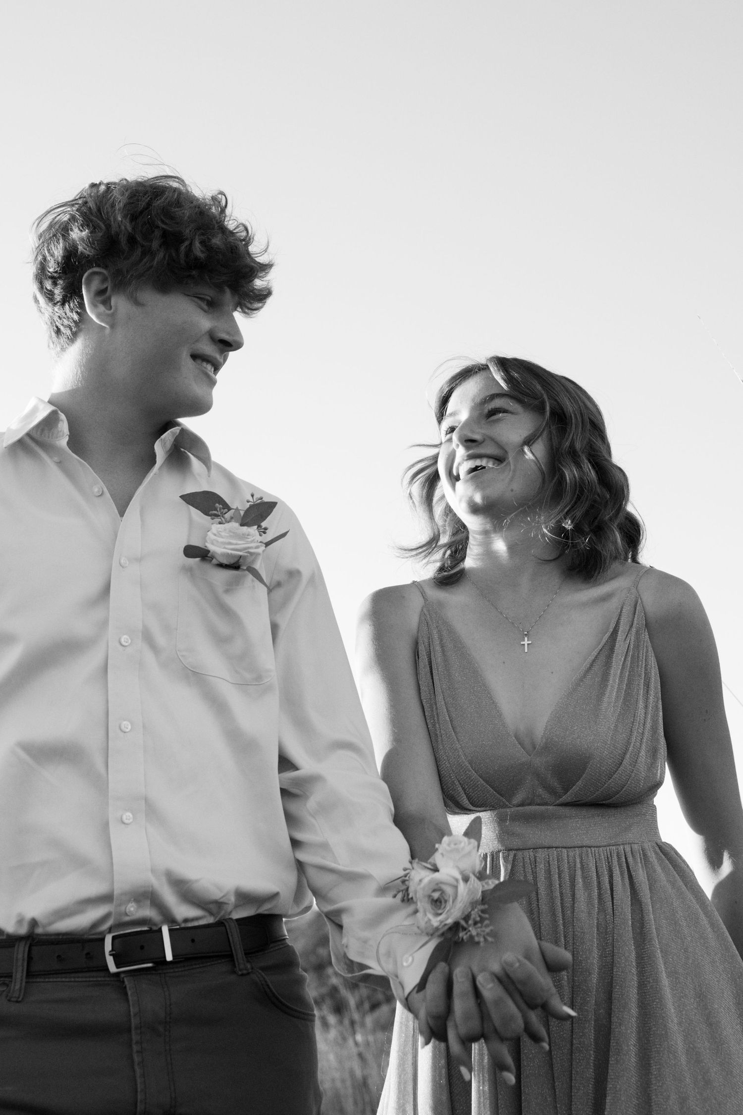 Black and white photo of a smiling couple holding hands, dressed in formal attire with boutonniere and corsage.