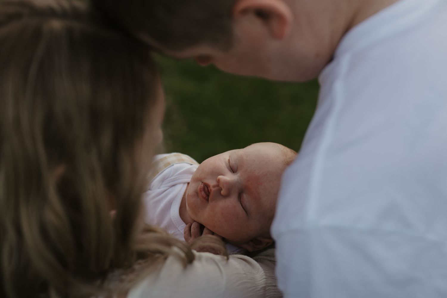 Parents lovingly gazing at their sleeping newborn baby outdoors in a tender family portrait.