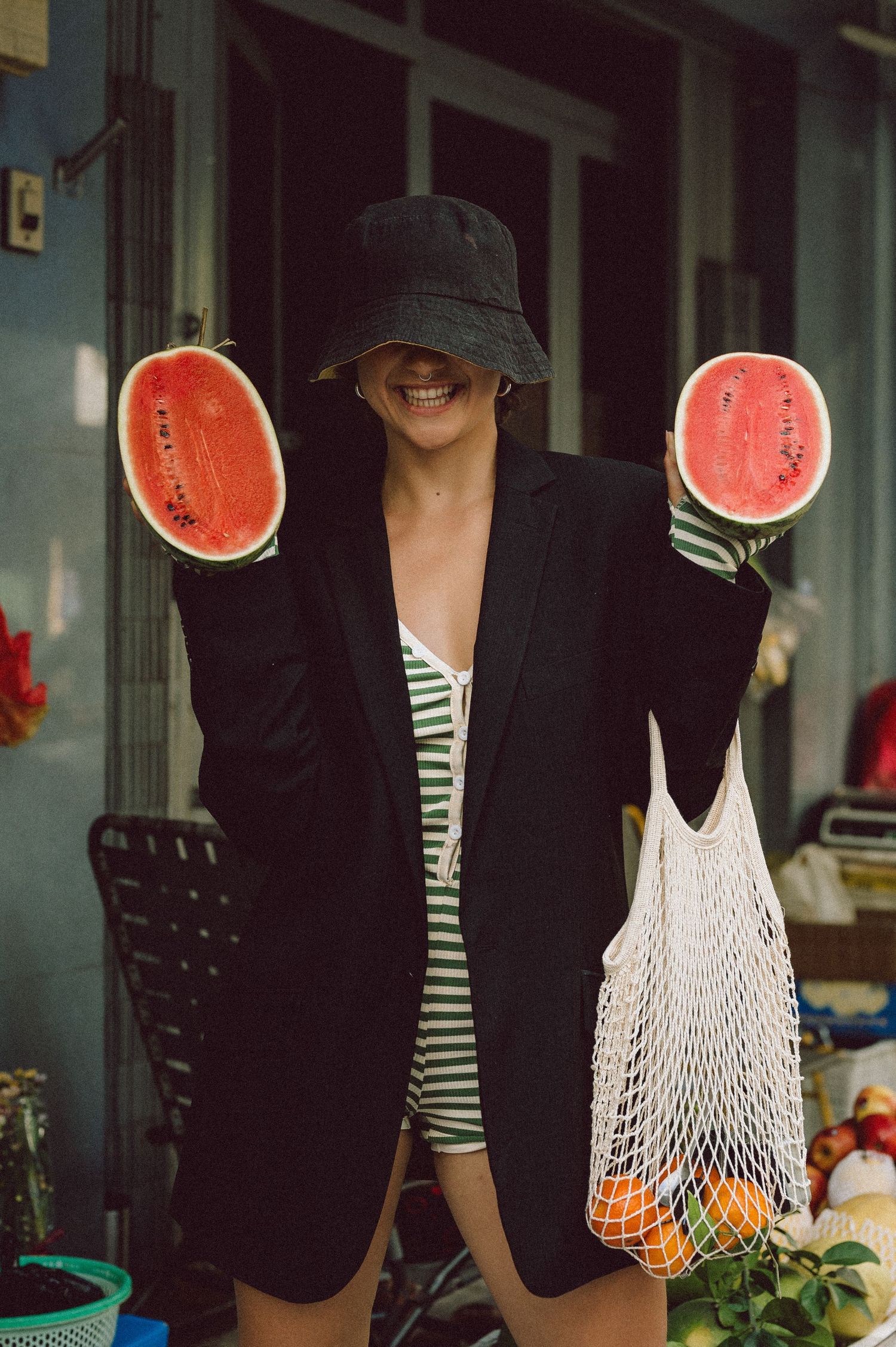 Editorial portrait of a woman holding two watermelon halves at Banana Garden Market, Ho Chi Minh City — street fashion photography by Anasta