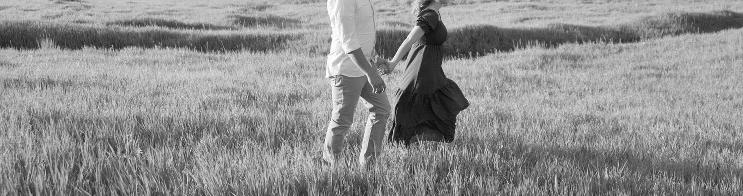 Black and white image of two people walking together through a tall grassy field.