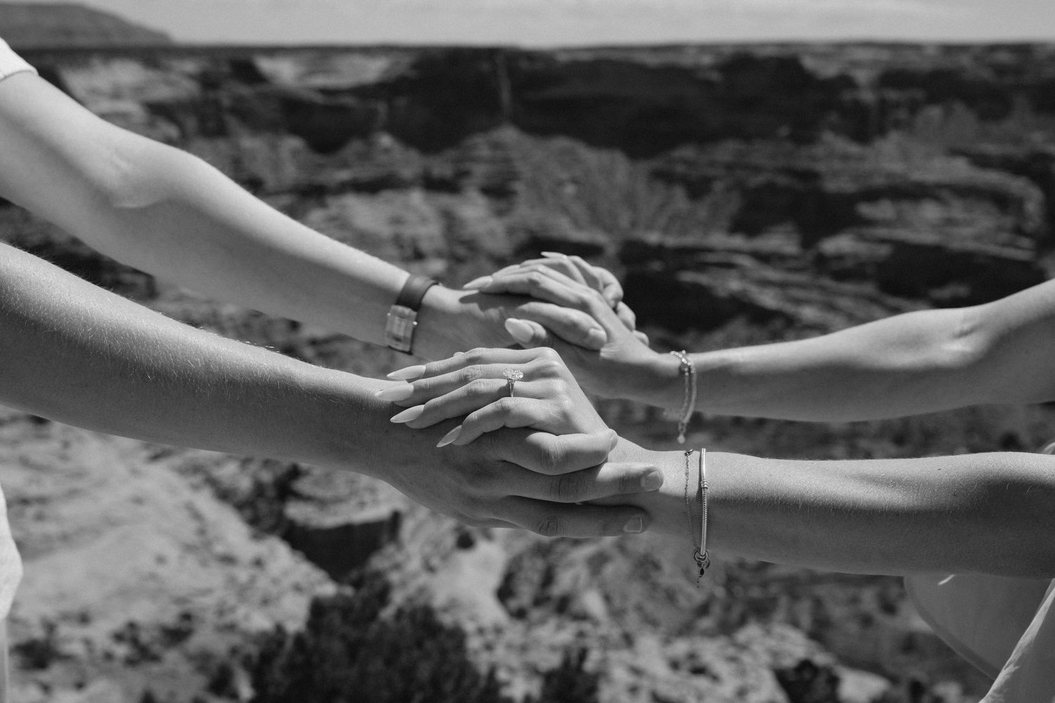 Hands reaching and clasping together against a dramatic canyon landscape backdrop in black and white.