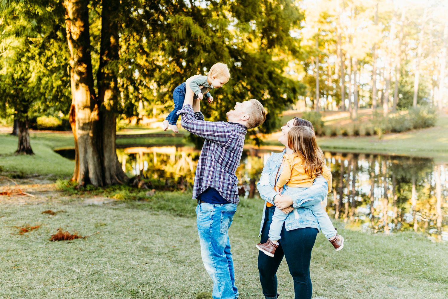 dad holds baby brother in the air while mom holds big sister and smiles behind them