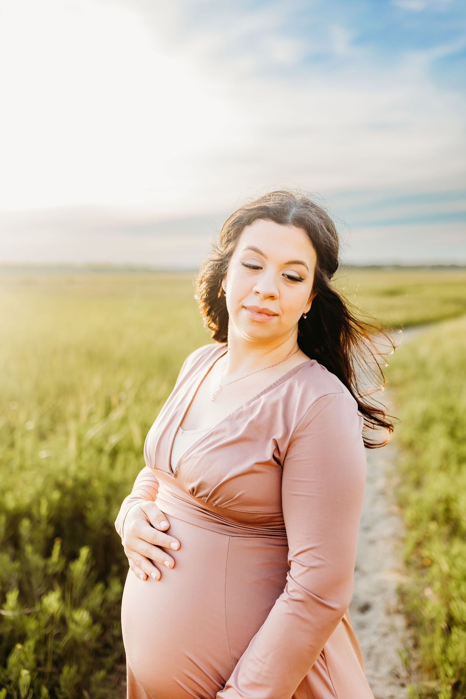 a pregnant mom holds her belly in the marsh