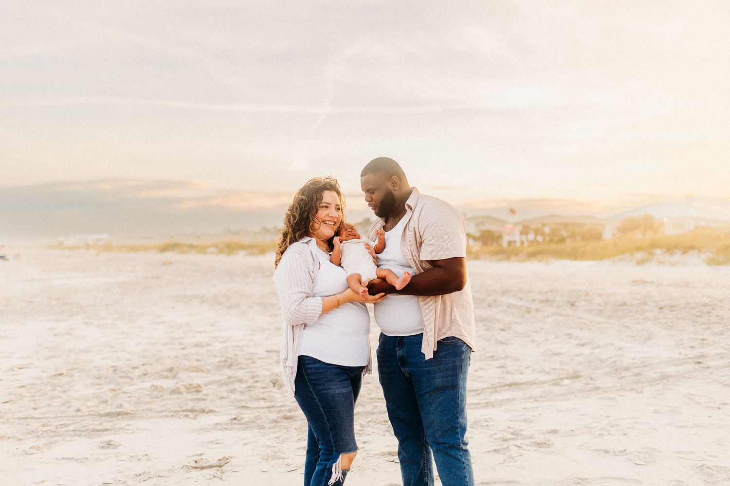 new parents hold their newborn baby boy on the beach
